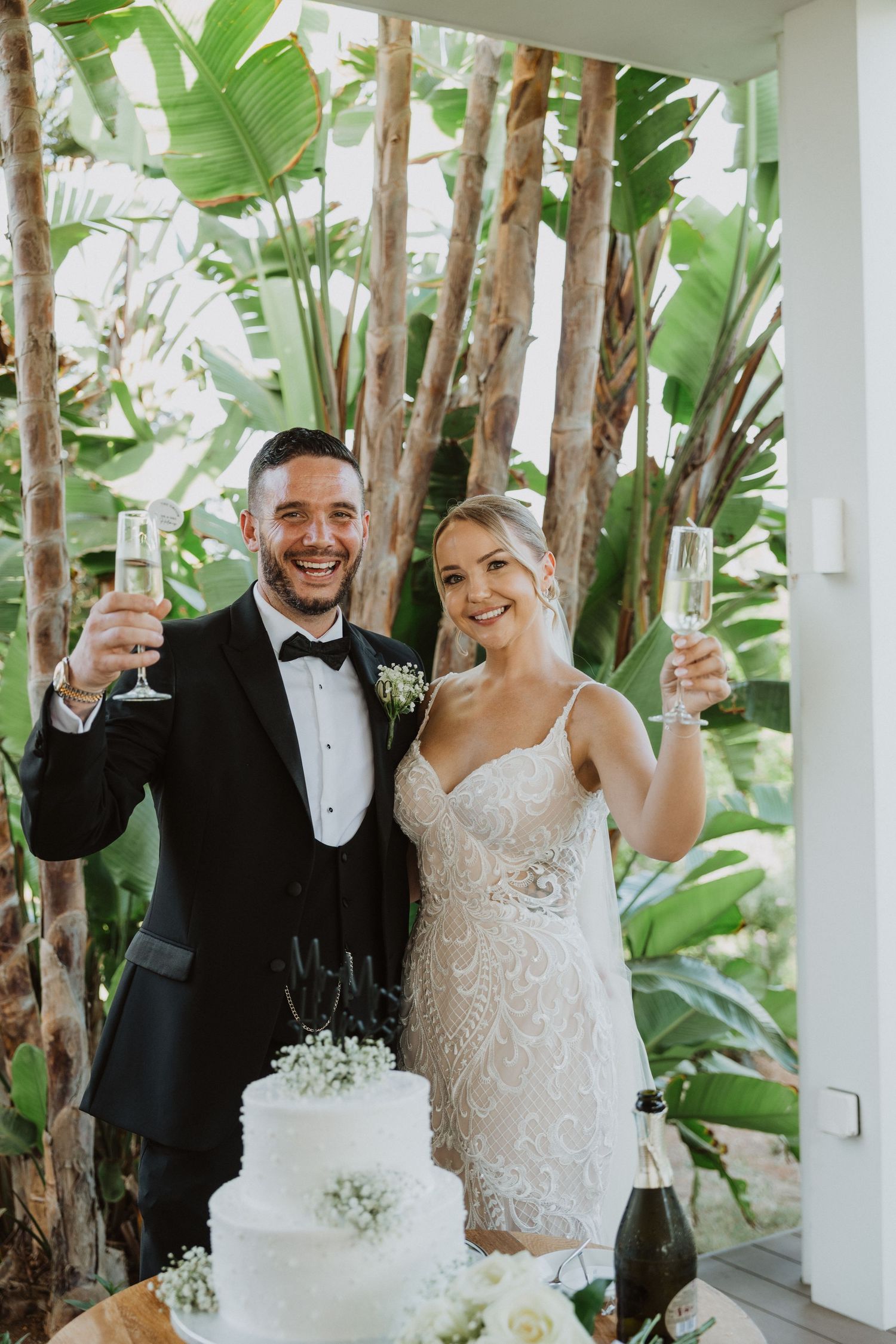 Wedding celebration with champagne toast and white cake on display in a tropical garden setting.