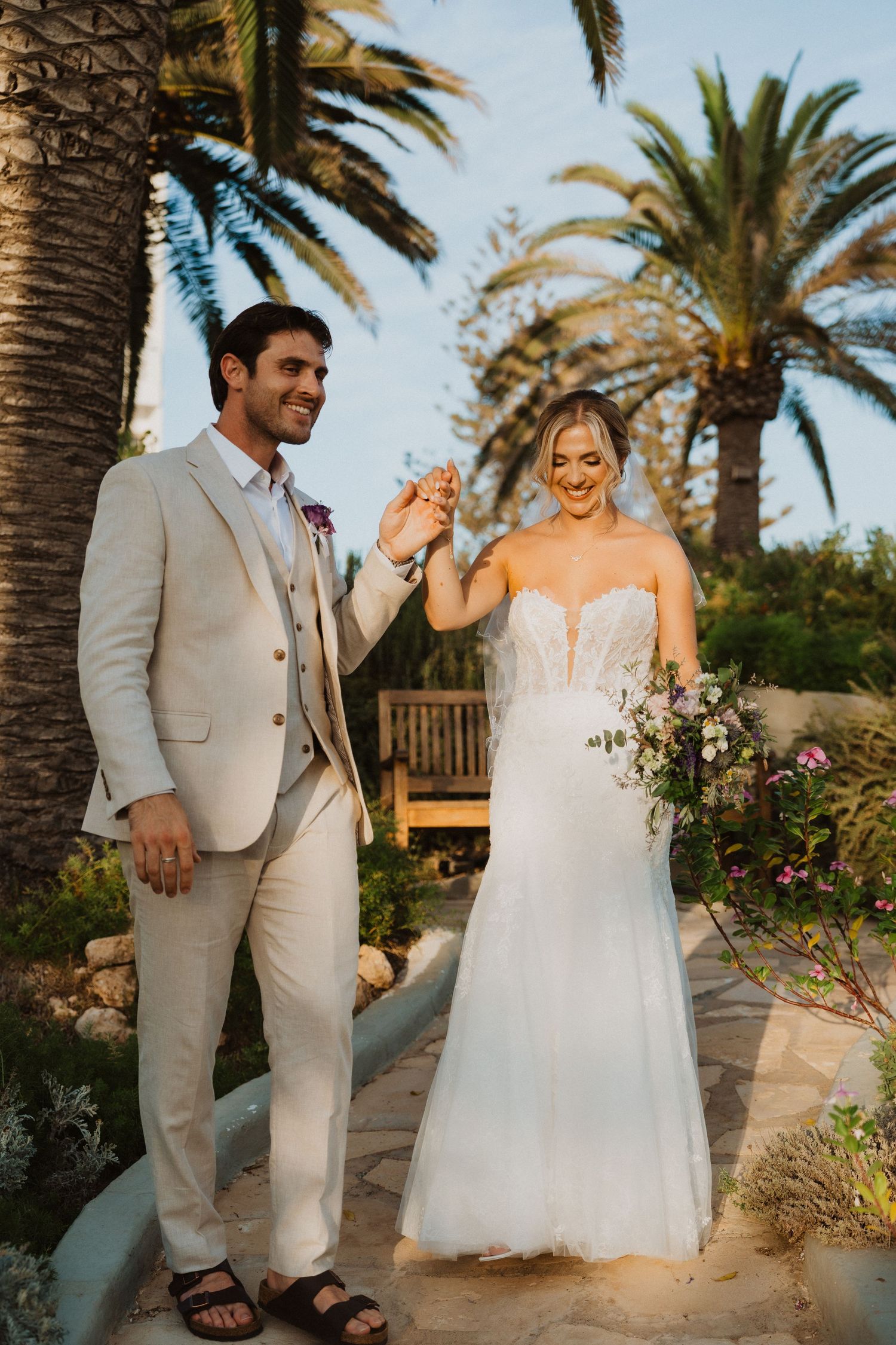 Joyful wedding couple celebrates under palm trees in a coastal garden setting.
