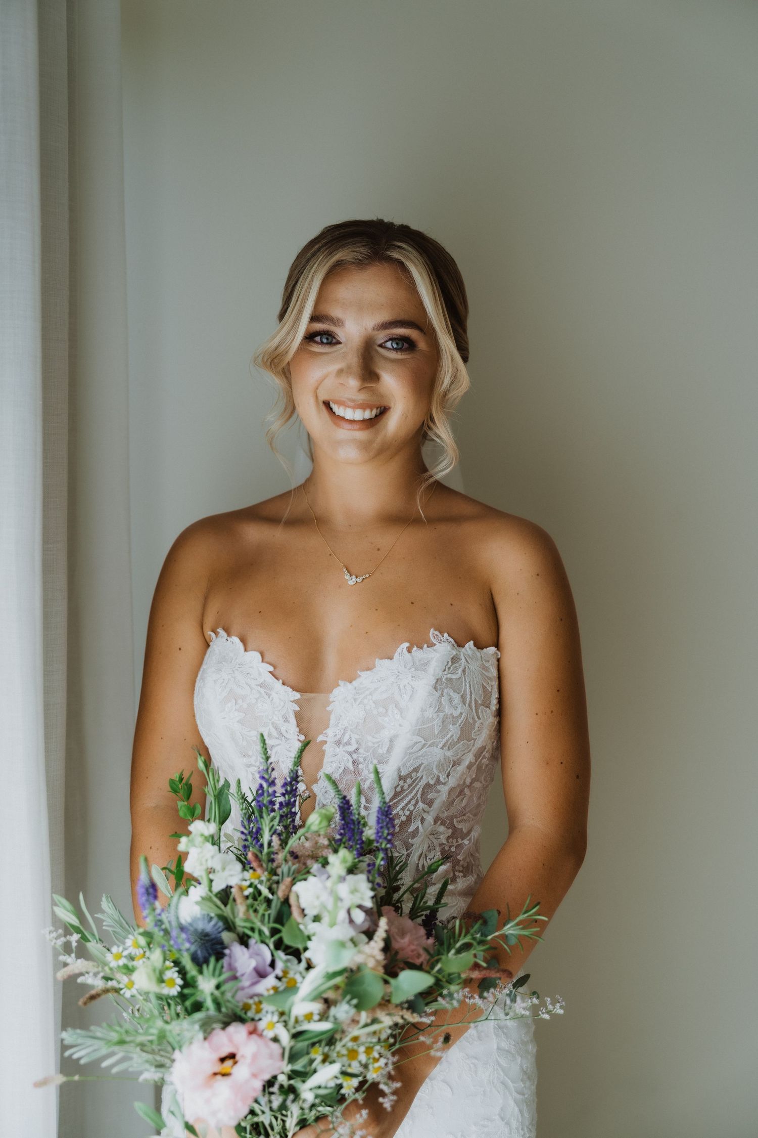 Radiant bride in strapless gown holding a garden-style bouquet with purple and white flowers.