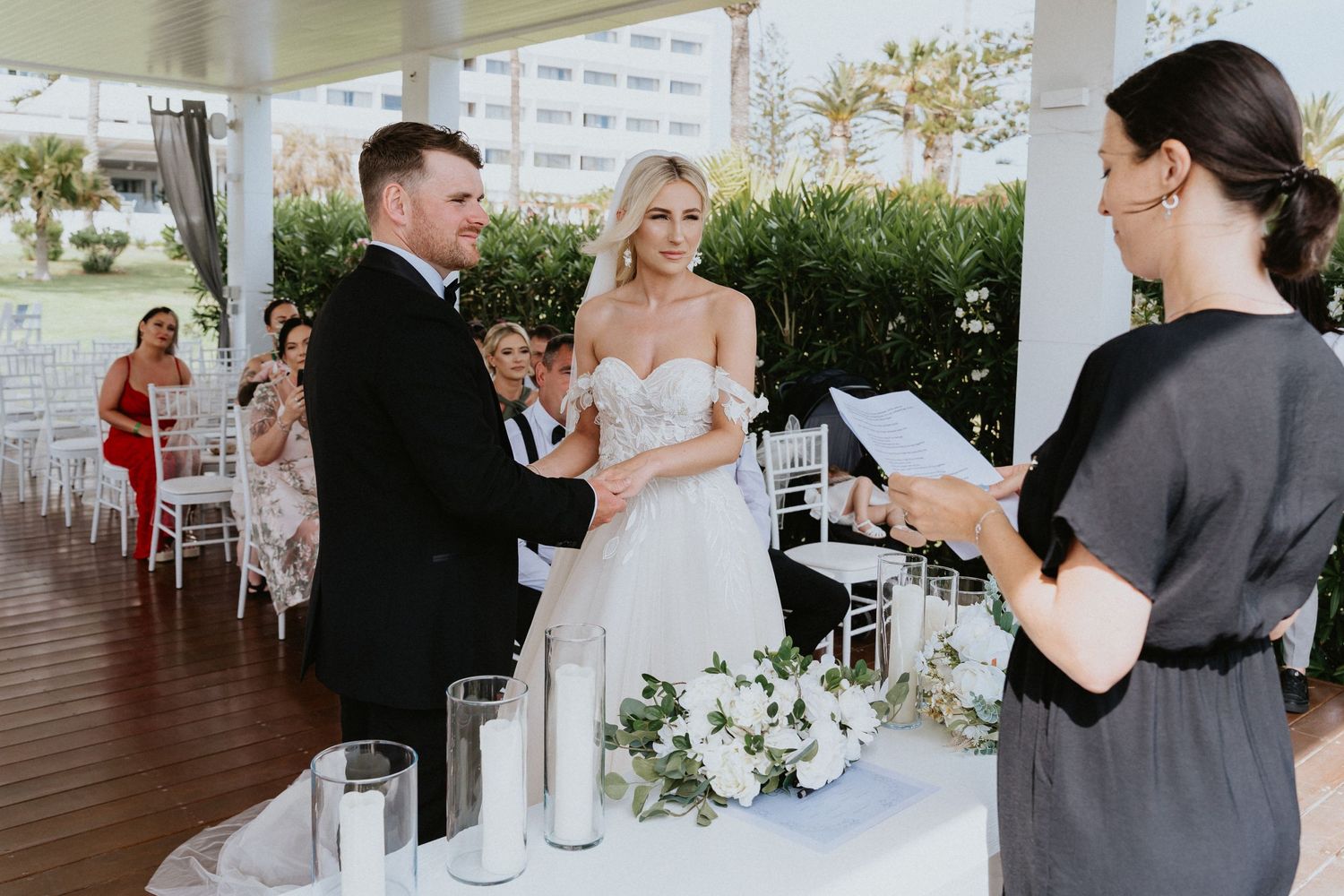 An outdoor wedding ceremony with white floral decorations and guests seated on a covered deck.