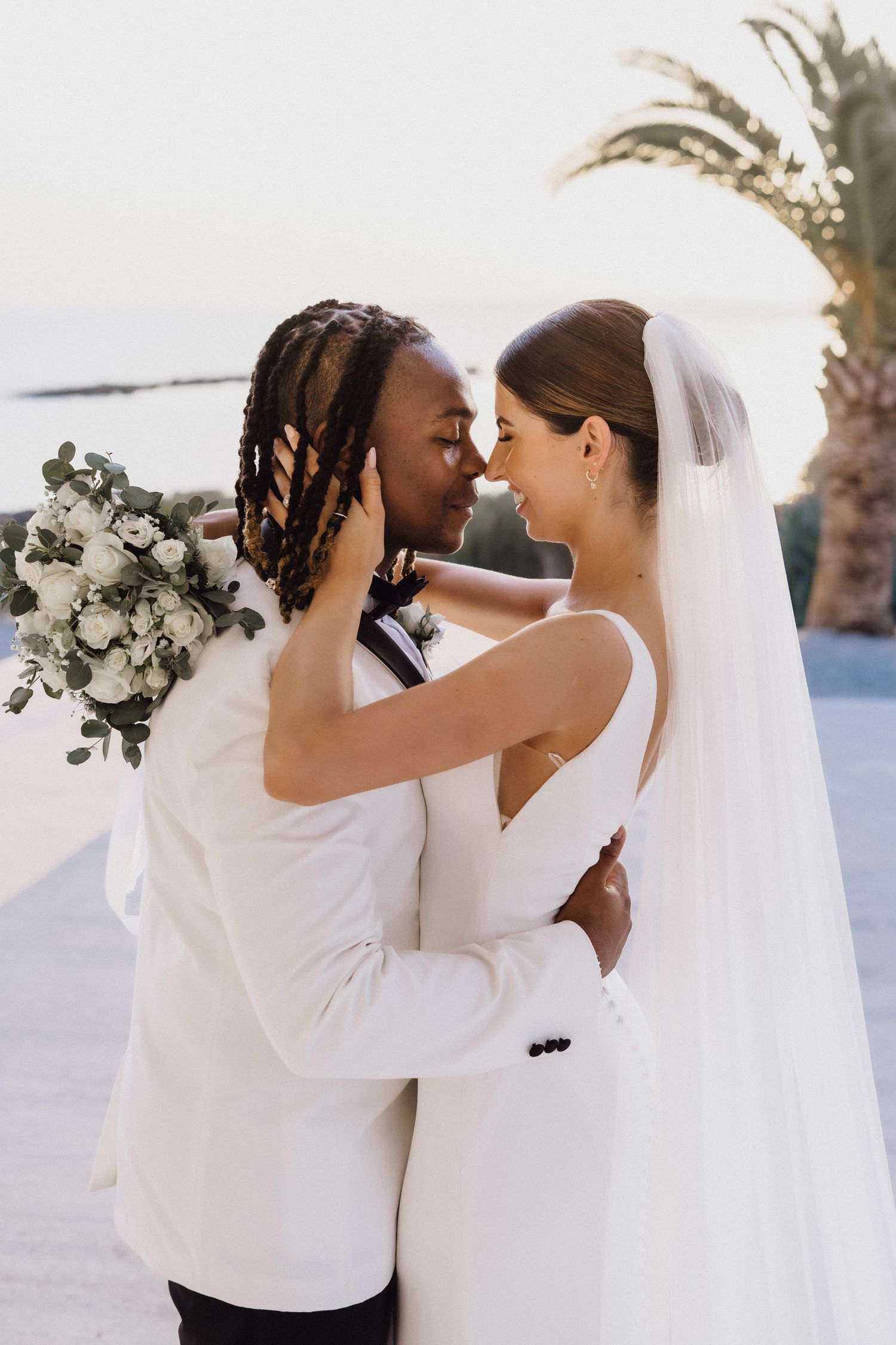 An intimate wedding portrait with white flowers and palm trees in a coastal setting.