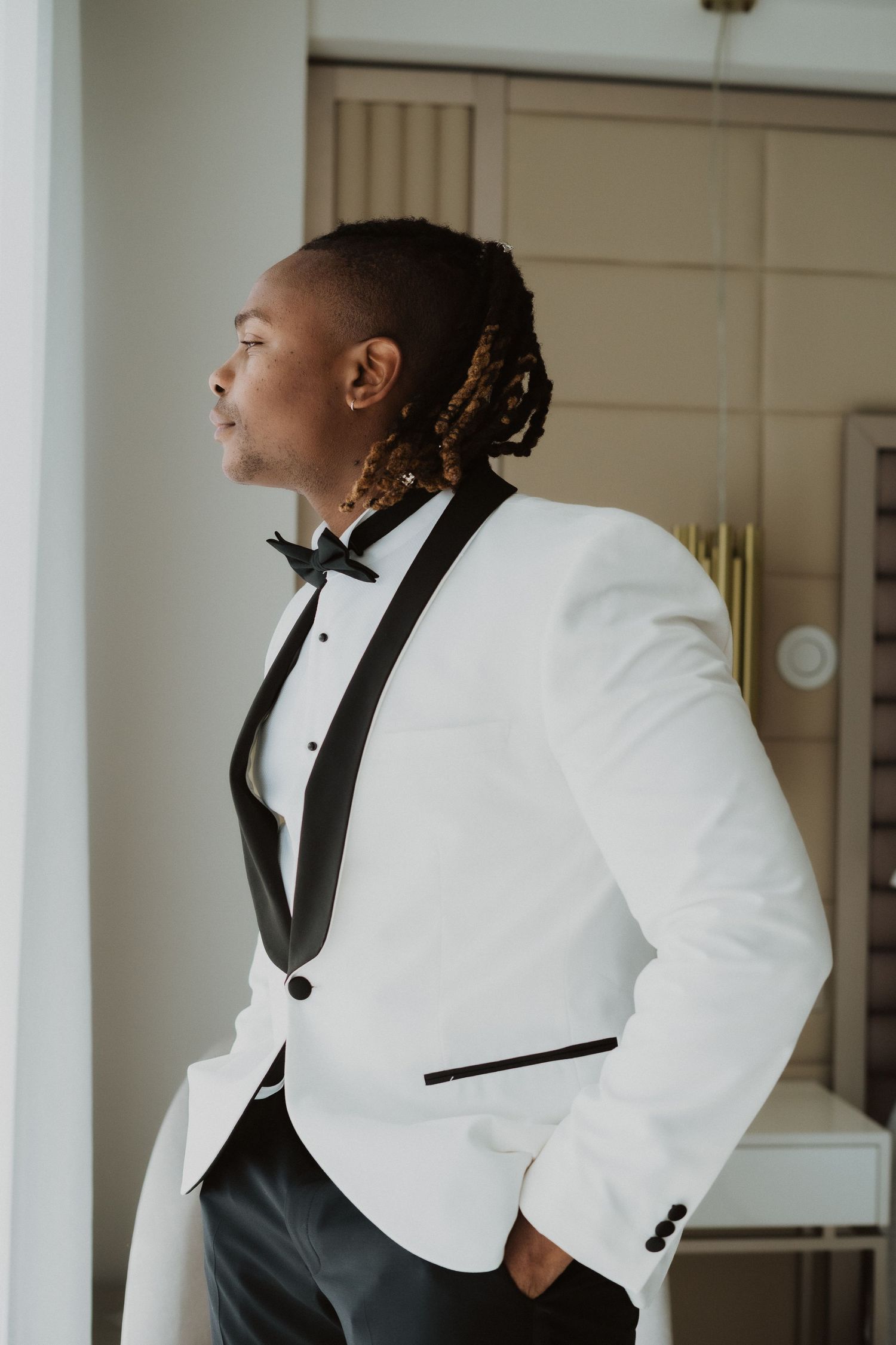 A profile shot of someone in a crisp white tuxedo looking towards natural light.