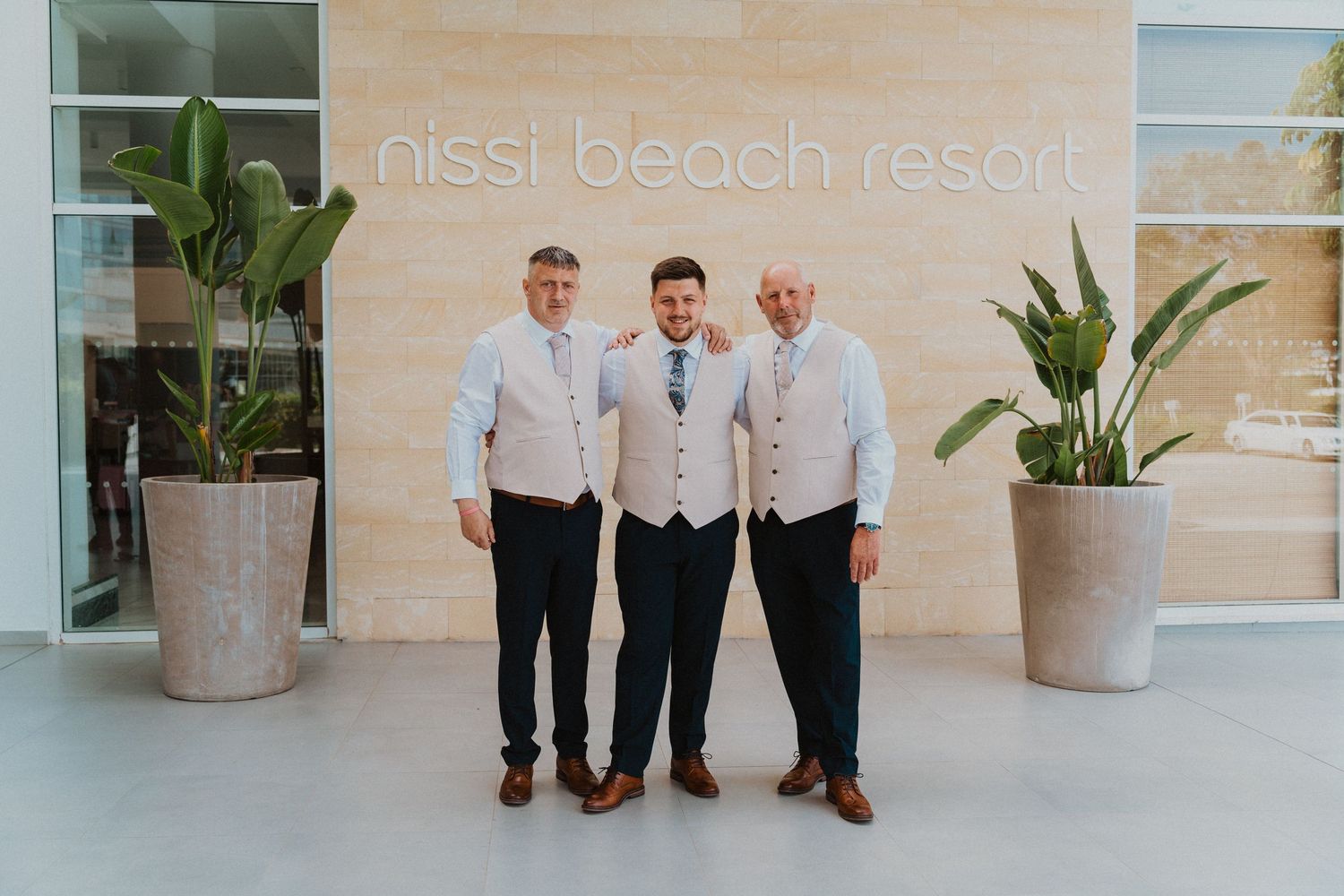 Three people in formal attire standing at Nissi Beach Resort entrance.