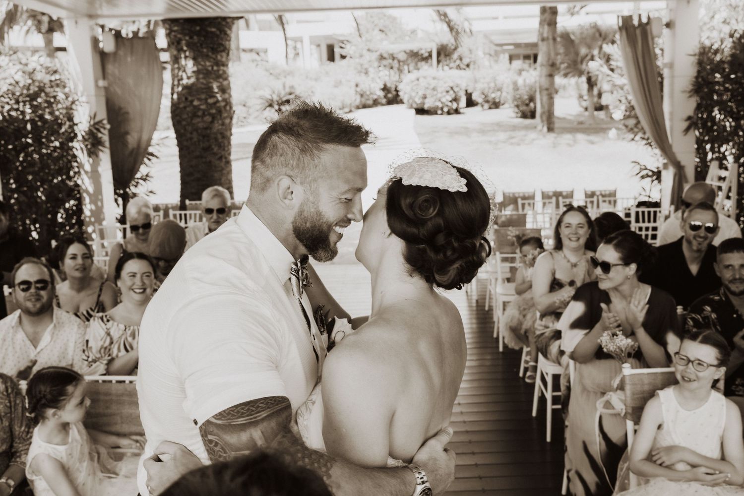 A sepia-toned capture of a romantic wedding ceremony moment on a covered outdoor patio.