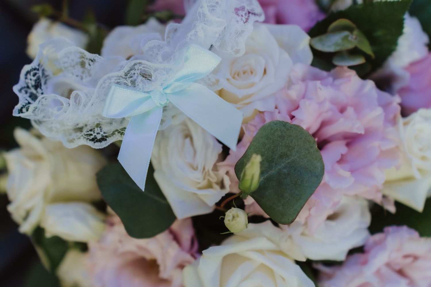 Delicate pink and white roses with eucalyptus leaves adorned with a light blue ribbon in a wedding bouquet.