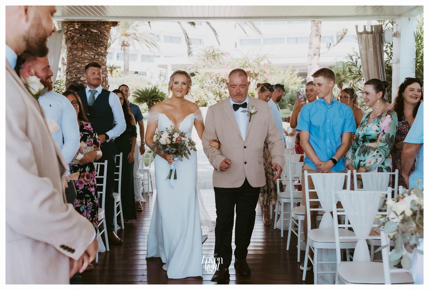 Wedding ceremony in white decorated venue with guests seated in white chairs.