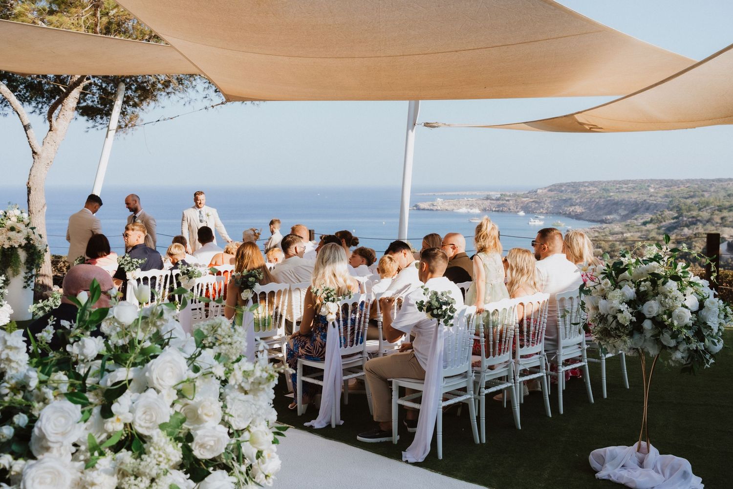Elegant outdoor wedding reception under white canopy tent with mountain views and white floral decorations.