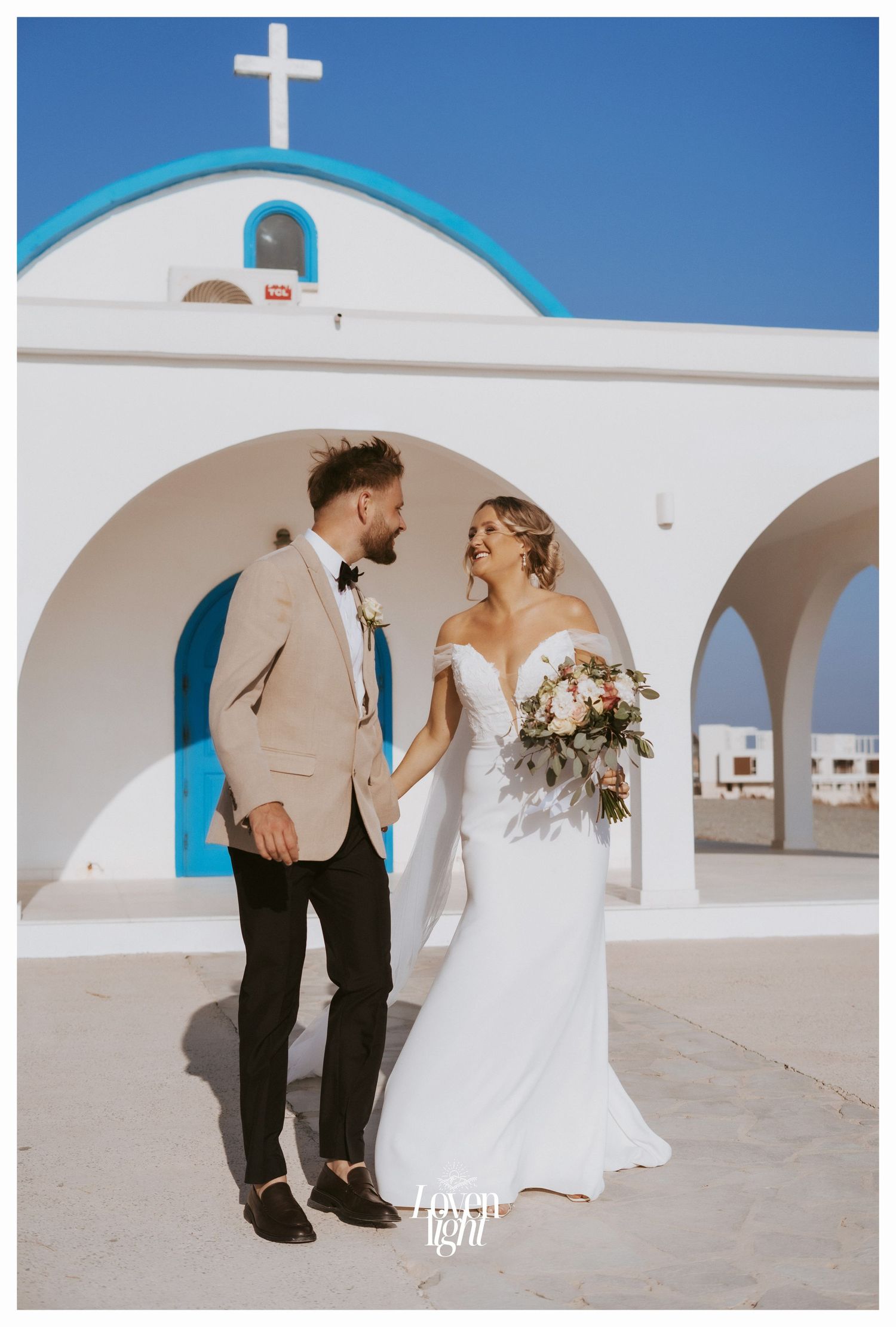 Elegant wedding photo at Mediterranean church with blue and white architectural details.