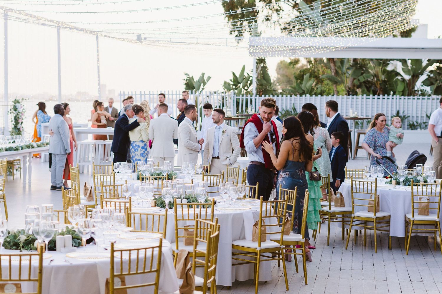 Elegant outdoor wedding reception setup with white tables and gold chairs under a tent.
