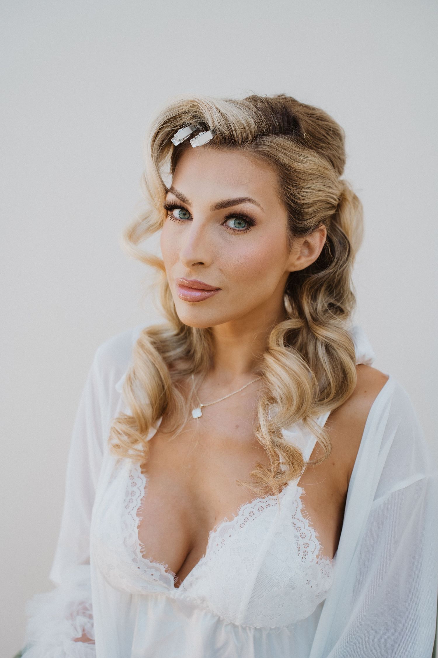 Elegant bridal portrait featuring soft blonde waves, delicate white lace lingerie and sheer robe in natural lighting.