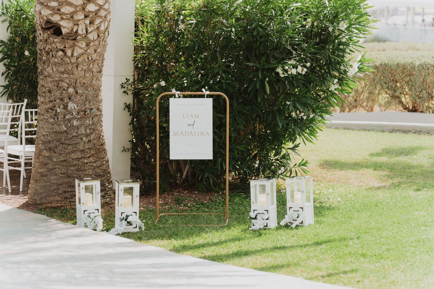 Outdoor wedding welcome sign display with gold frame and white lanterns on green lawn.