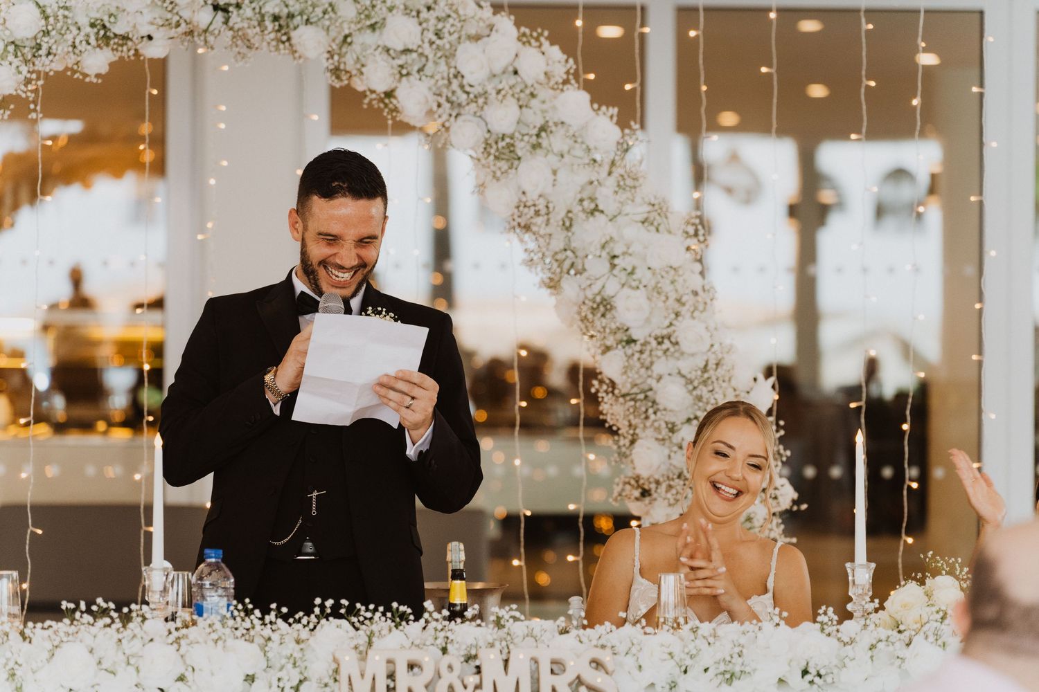 Wedding celebration with white floral arch decorations and hanging fairy lights creating a romantic atmosphere.