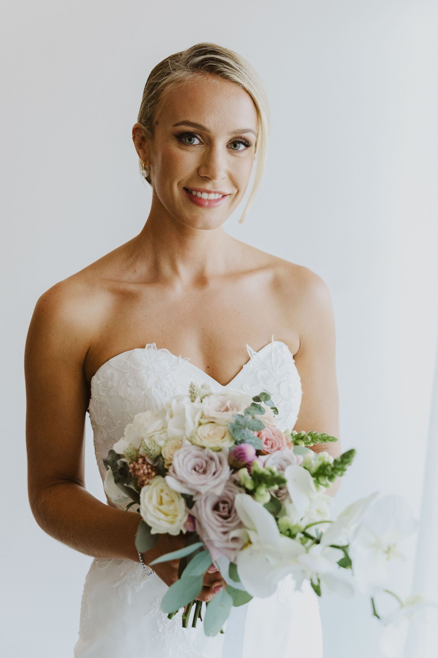 Radiant bride in strapless wedding gown holding elegant pastel bouquet against white background.