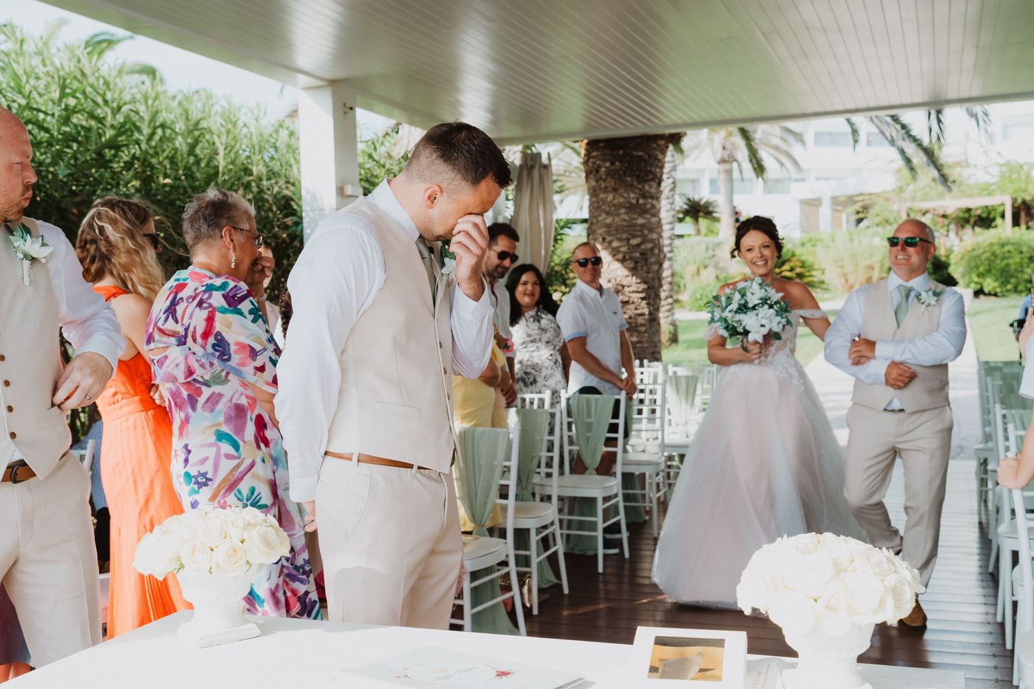 A joyful moment captured during an outdoor wedding celebration under a covered porch with tropical greenery.