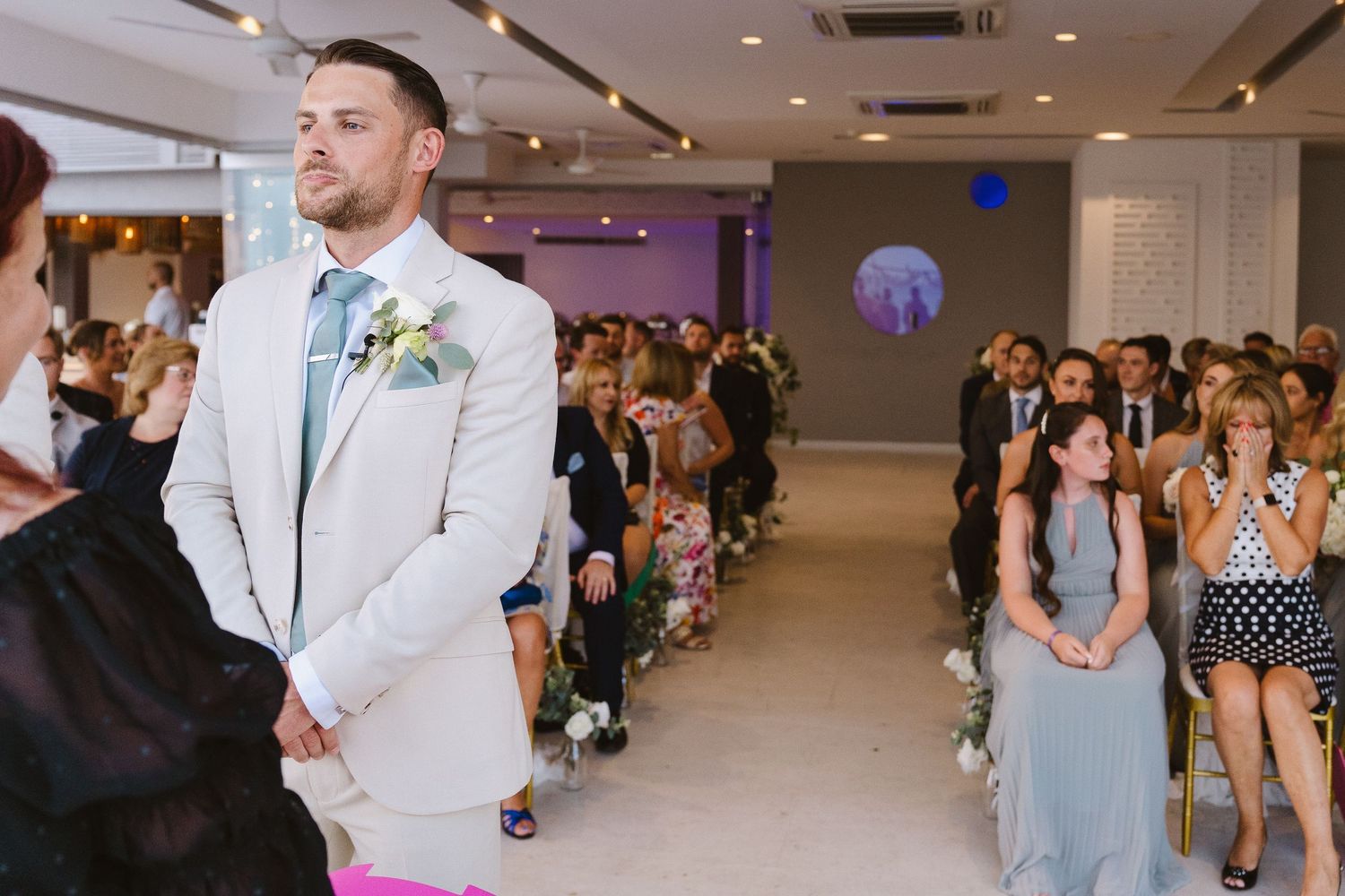 Modern indoor wedding ceremony with guests seated along a white aisle runner.