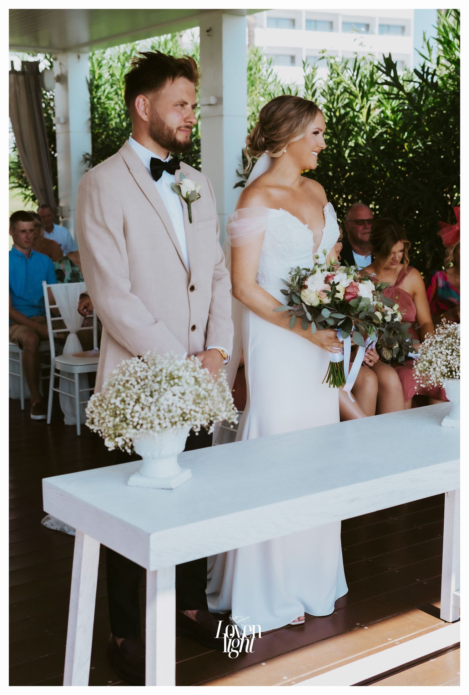 Formal wedding ceremony setup with white table and floral arrangements in outdoor pavilion.