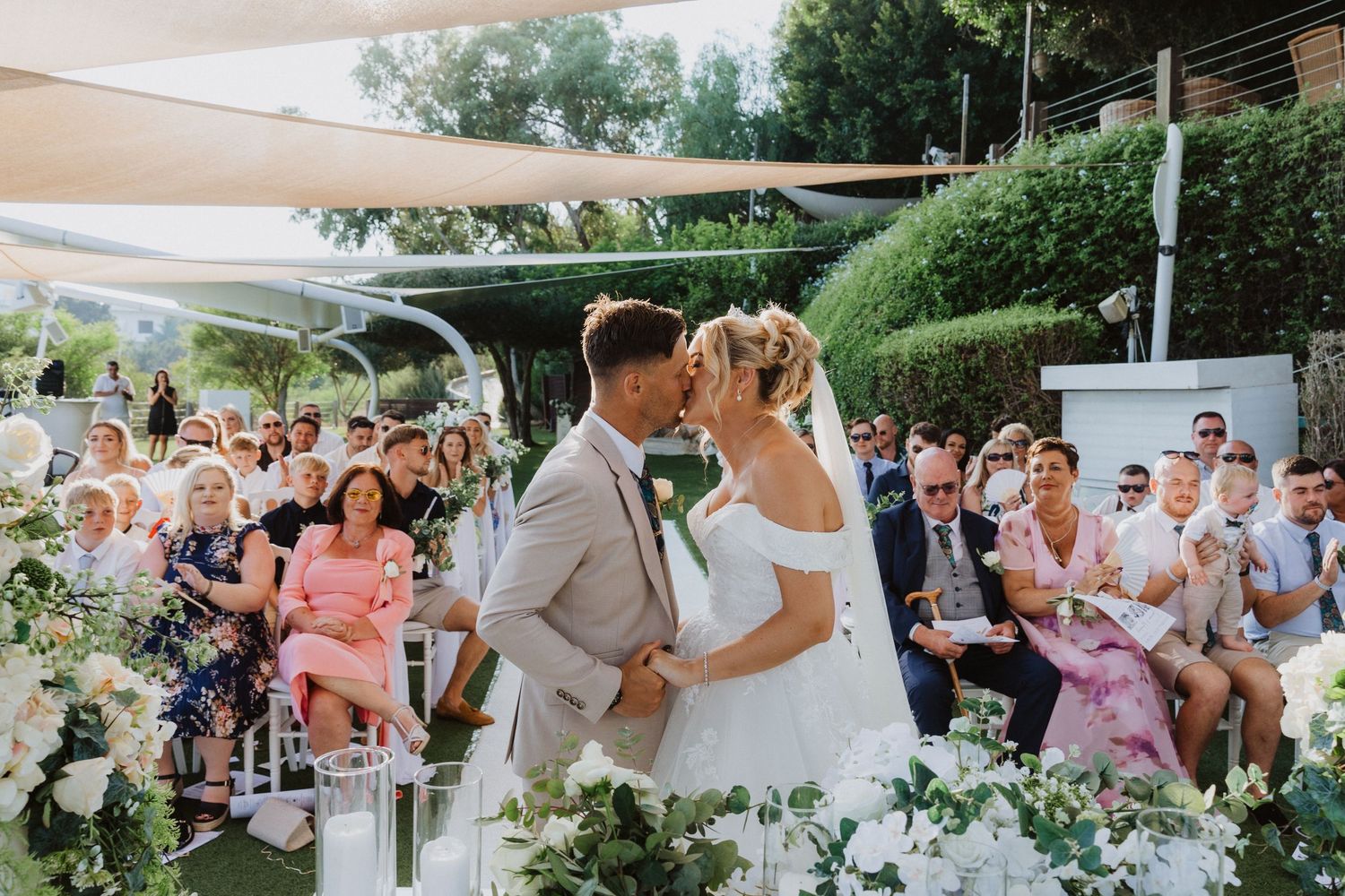 Beautiful outdoor wedding celebration with couple surrounded by pink and white floral decorations and seated guests.