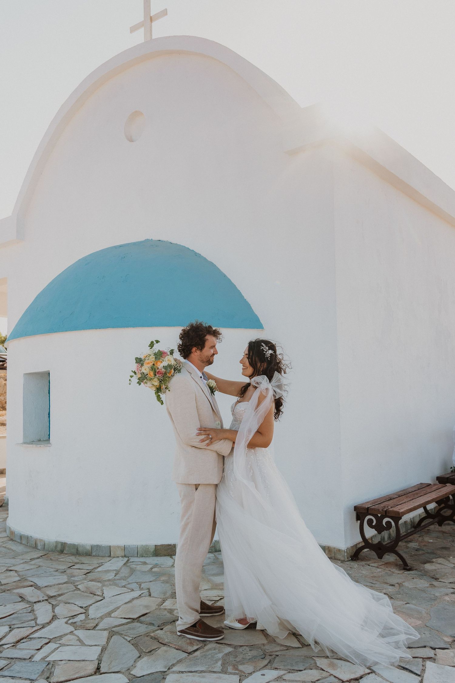 Romantic wedding portrait against iconic white Greek chapel with blue dome.