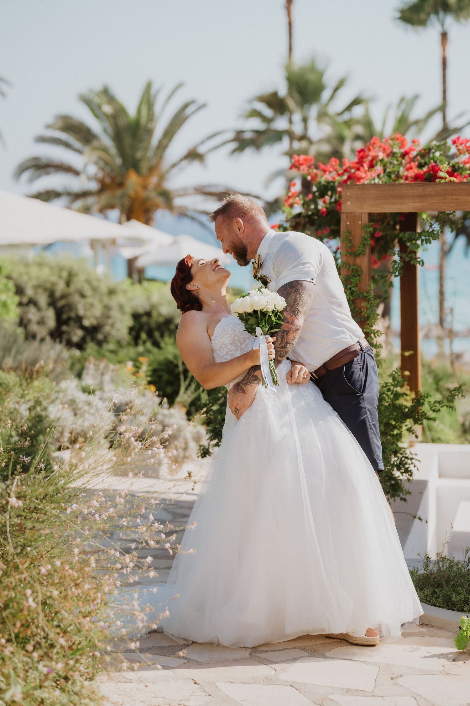 Romantic wedding moment captured in tropical garden setting with palm trees and floral decor.