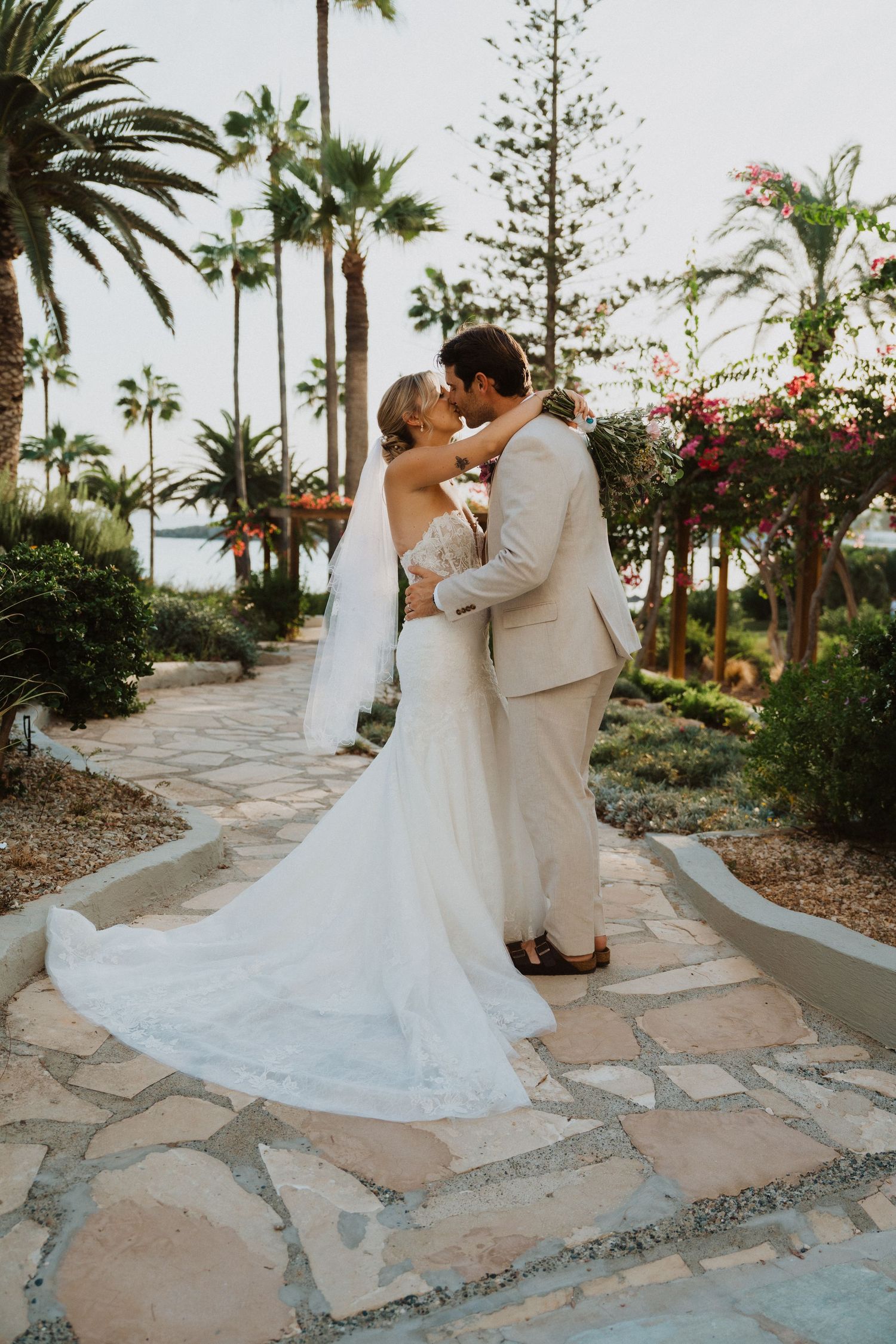 Newlyweds share a romantic dance on stone pathways surrounded by palm trees.
