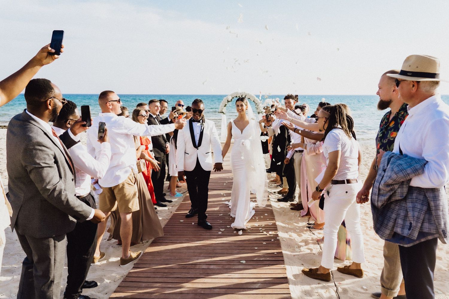 Wedding guests lining the boardwalk aisle capturing photos of the ceremony.