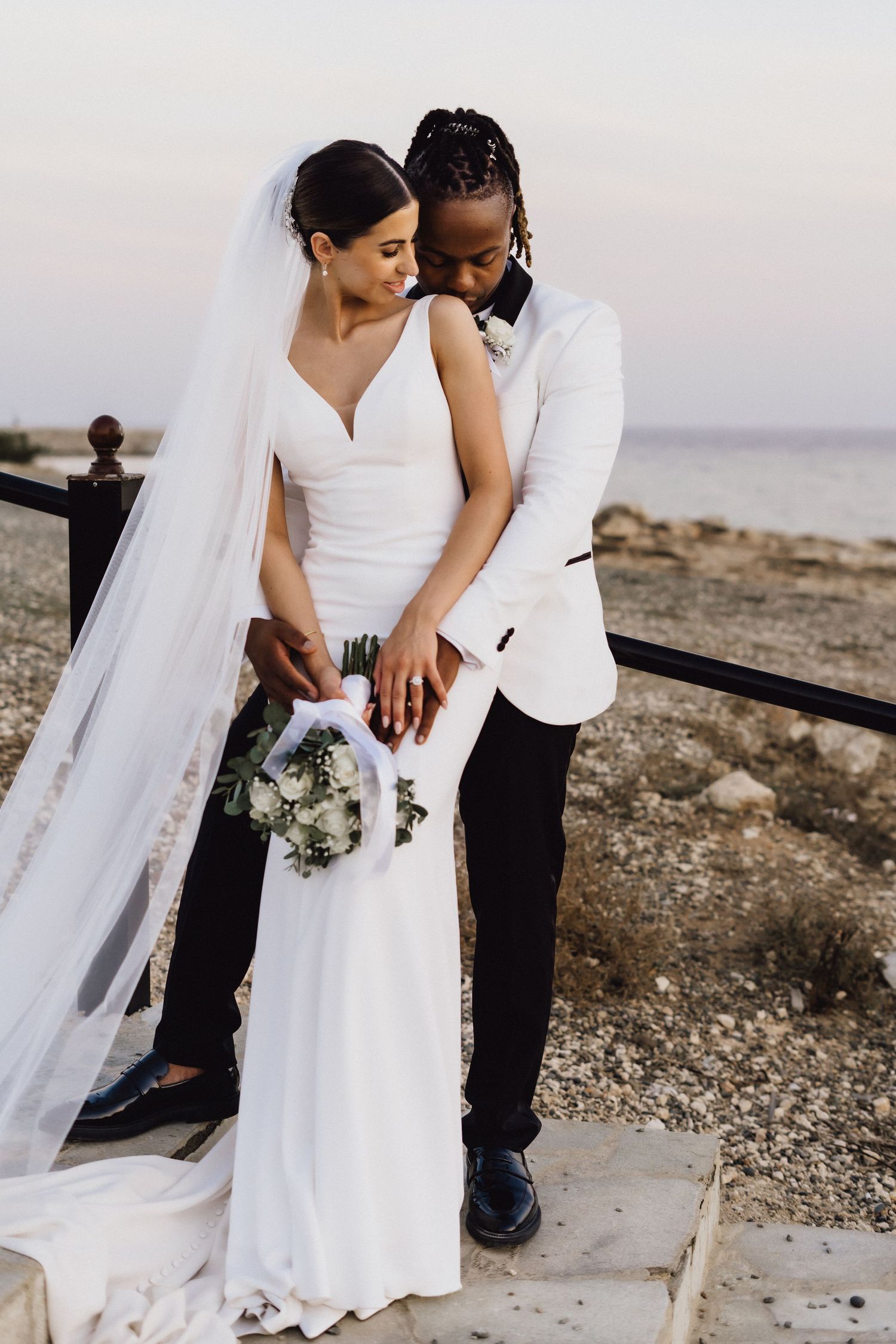 Tender wedding moment captured on coastal stone path with ocean view.