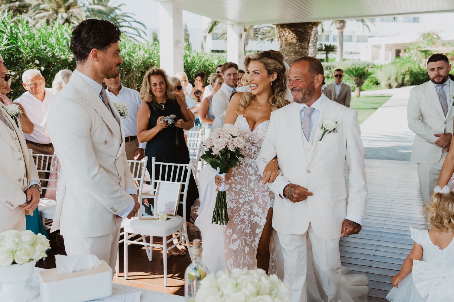 Wedding guests in white attire celebrate and dance together at an outdoor reception venue.