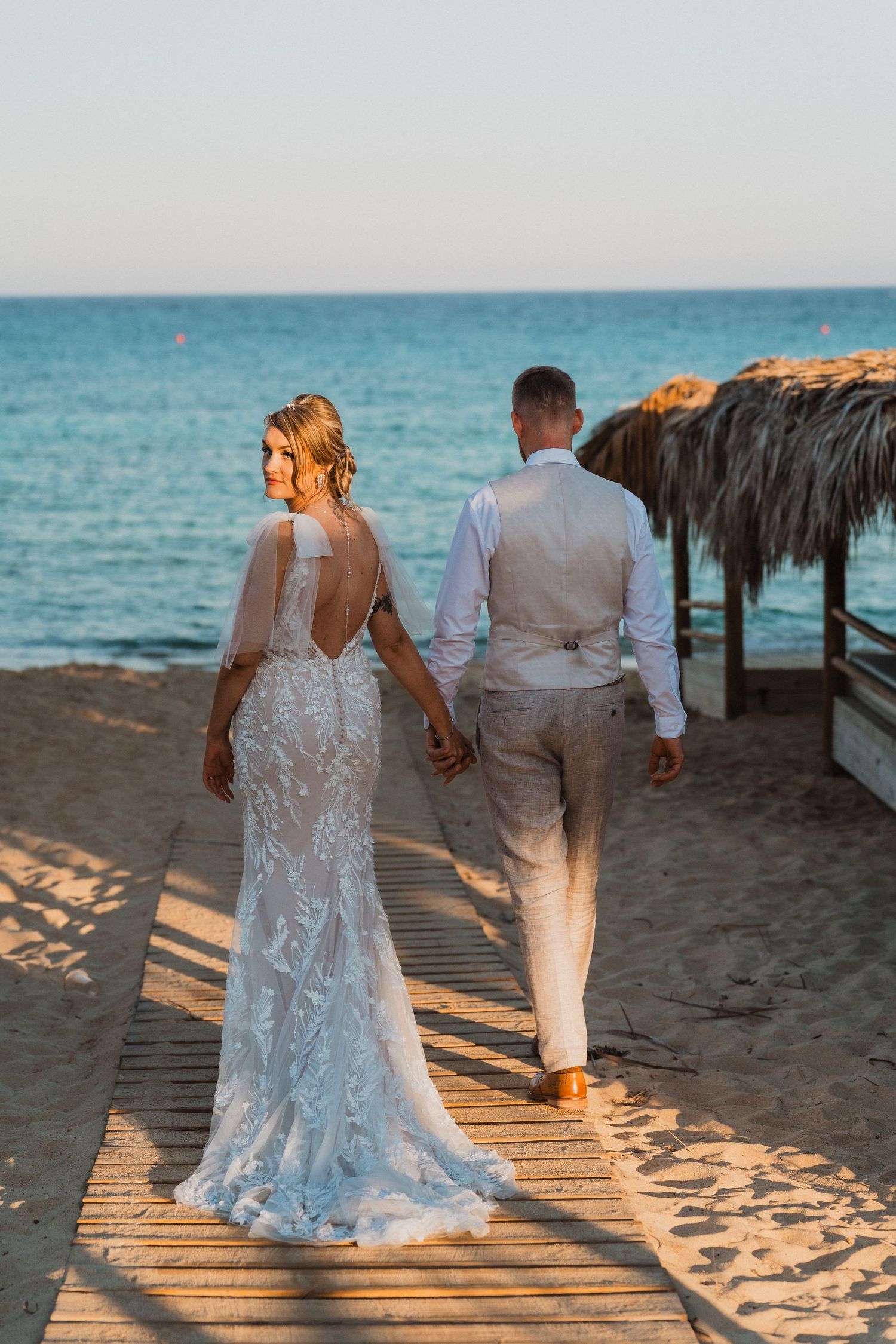 Newlyweds strolling hand in hand on beach boardwalk.