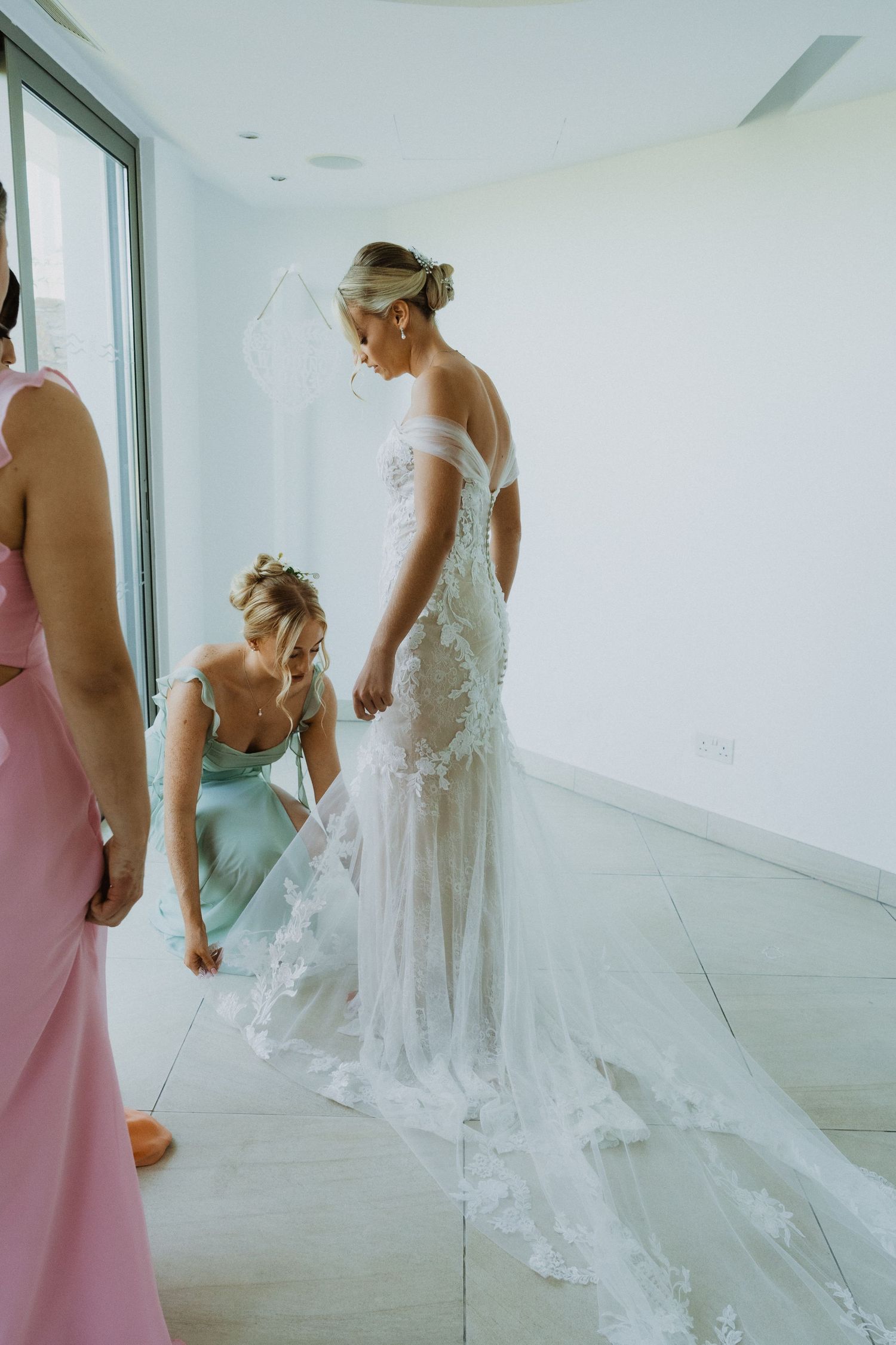 Wedding preparation scene showing flowing white dress details in a bright room.