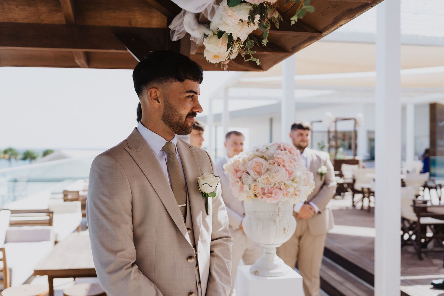 Wedding party members in formal attire gather under a covered wooden pavilion.