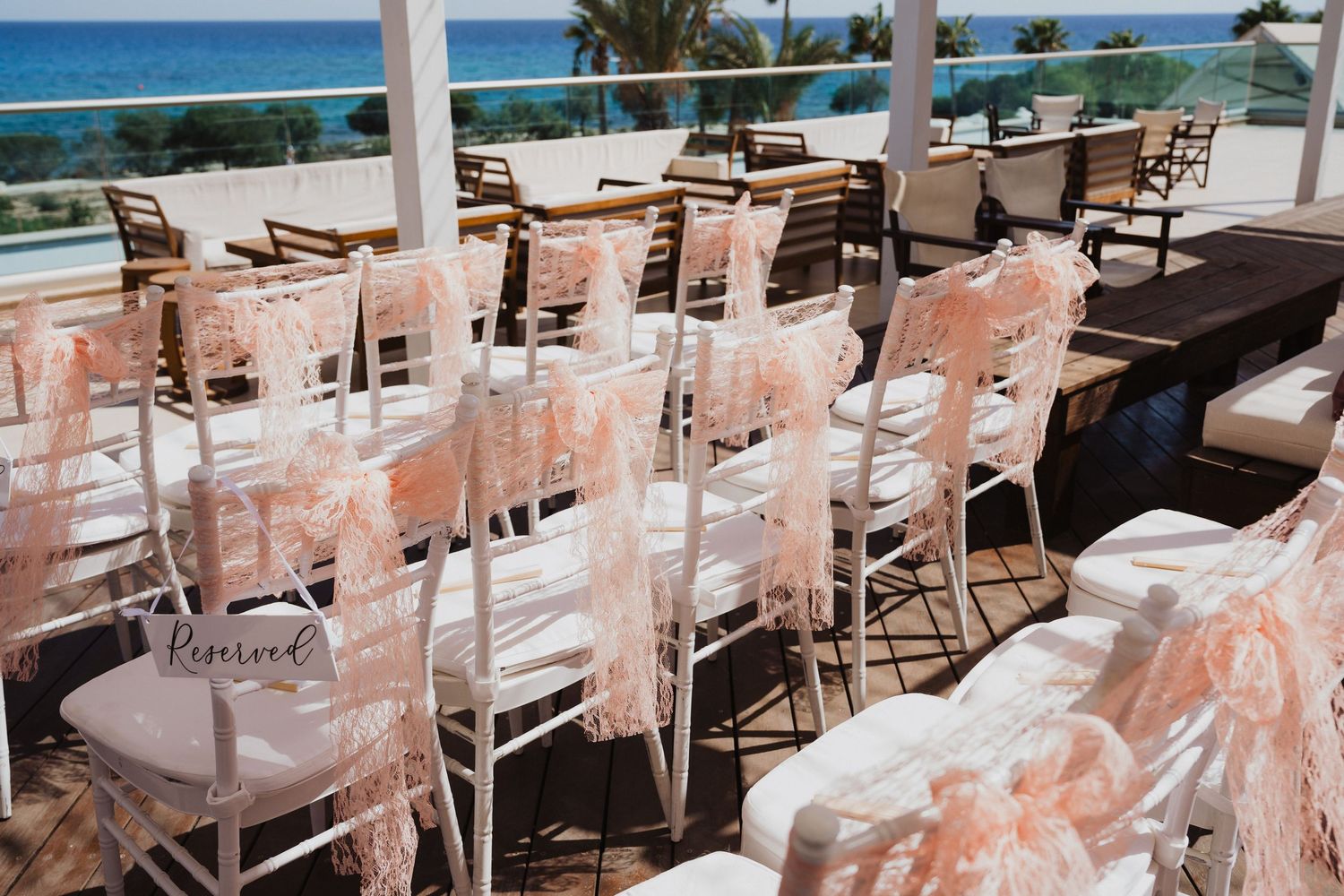 Oceanfront wedding setup with white chairs and peach accents under covered pavilions.