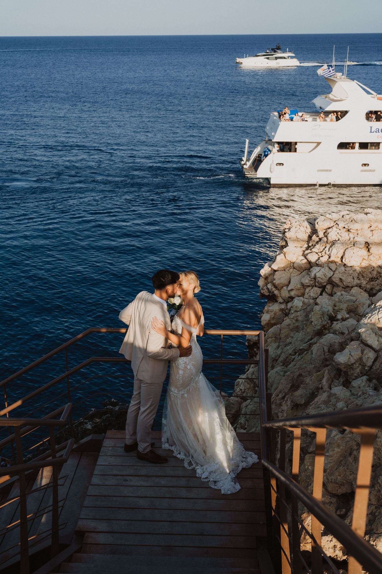Sunset wedding photography session on Mediterranean coastal boardwalk with passing boats.