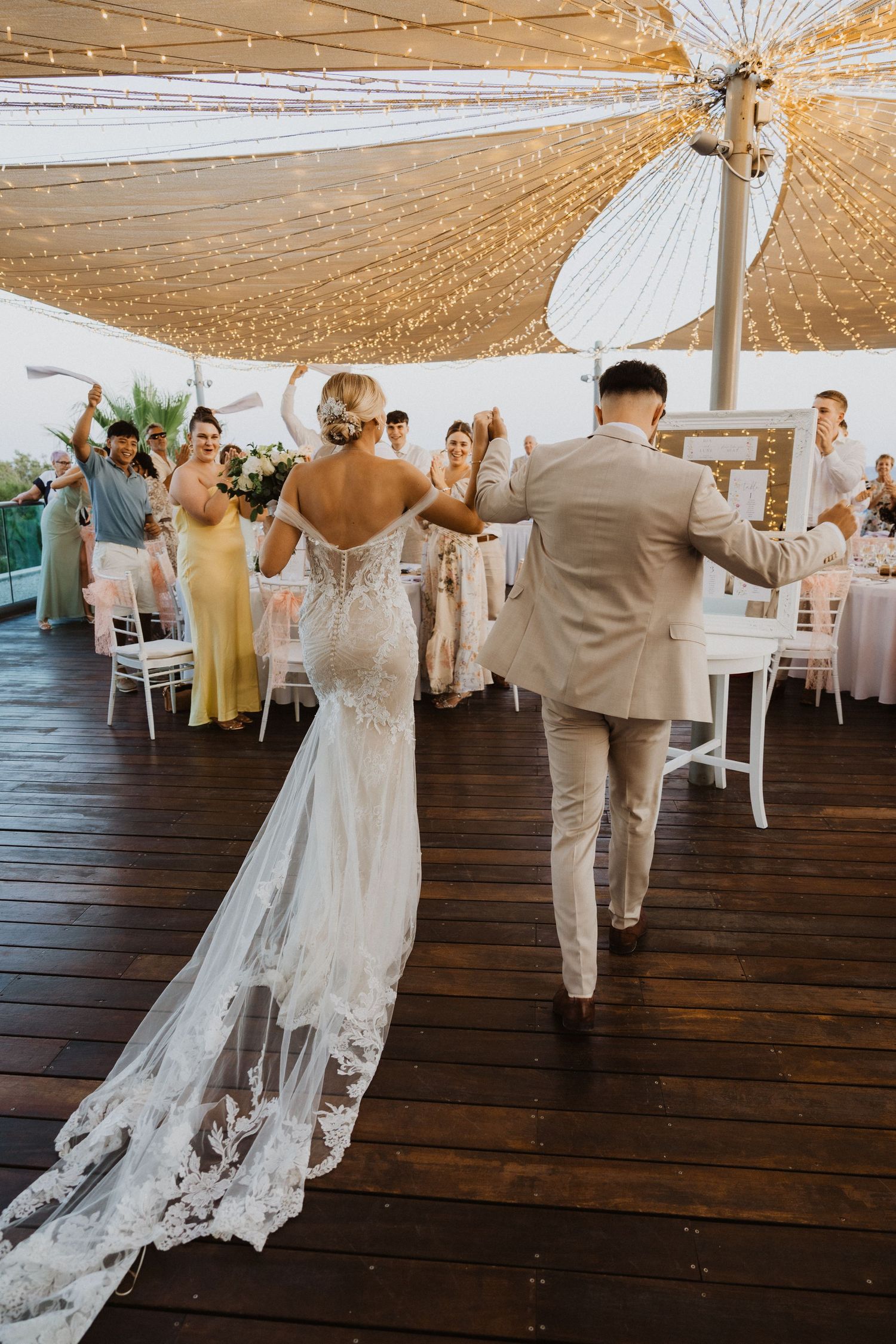 Wedding celebration under golden fabric canopy on wooden deck.
