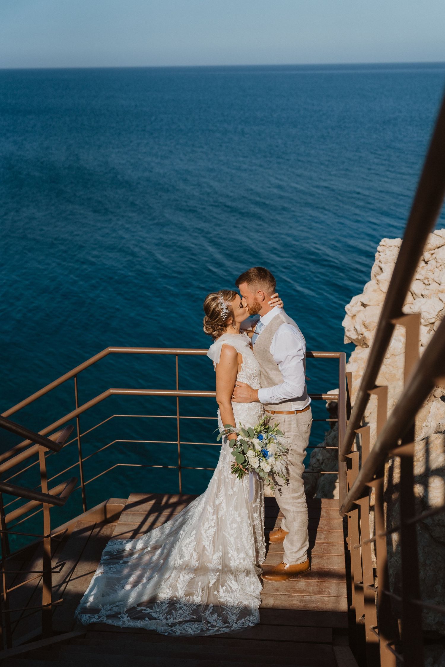 Romantic moment between newlyweds on oceanside wooden staircase.