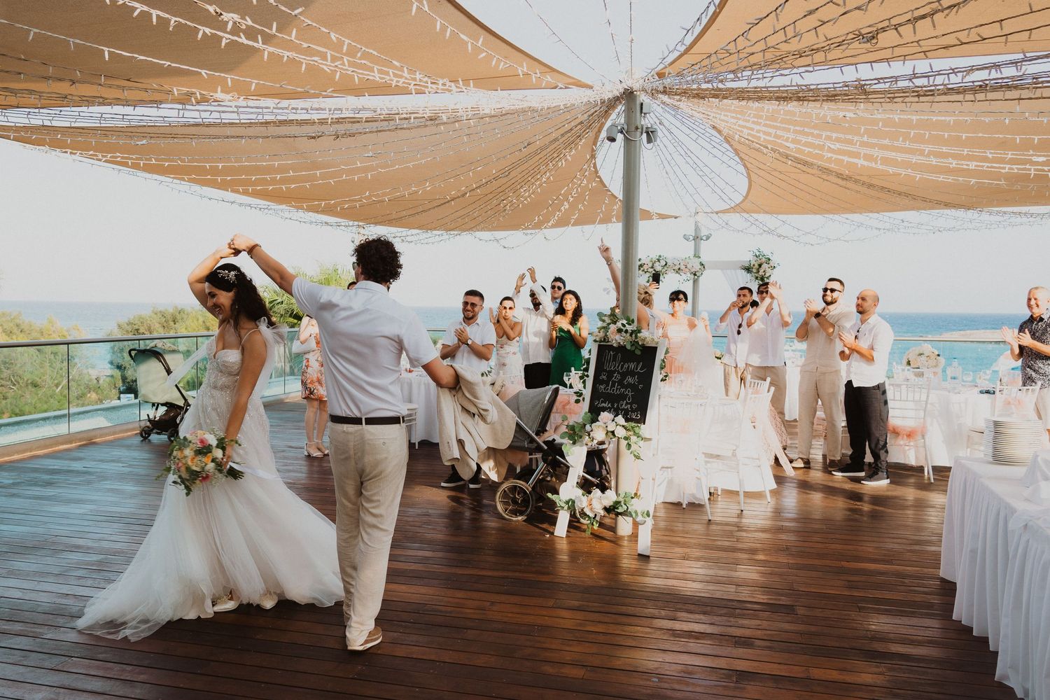 Wedding celebration on oceanfront deck with draped fabric canopy and string lights.