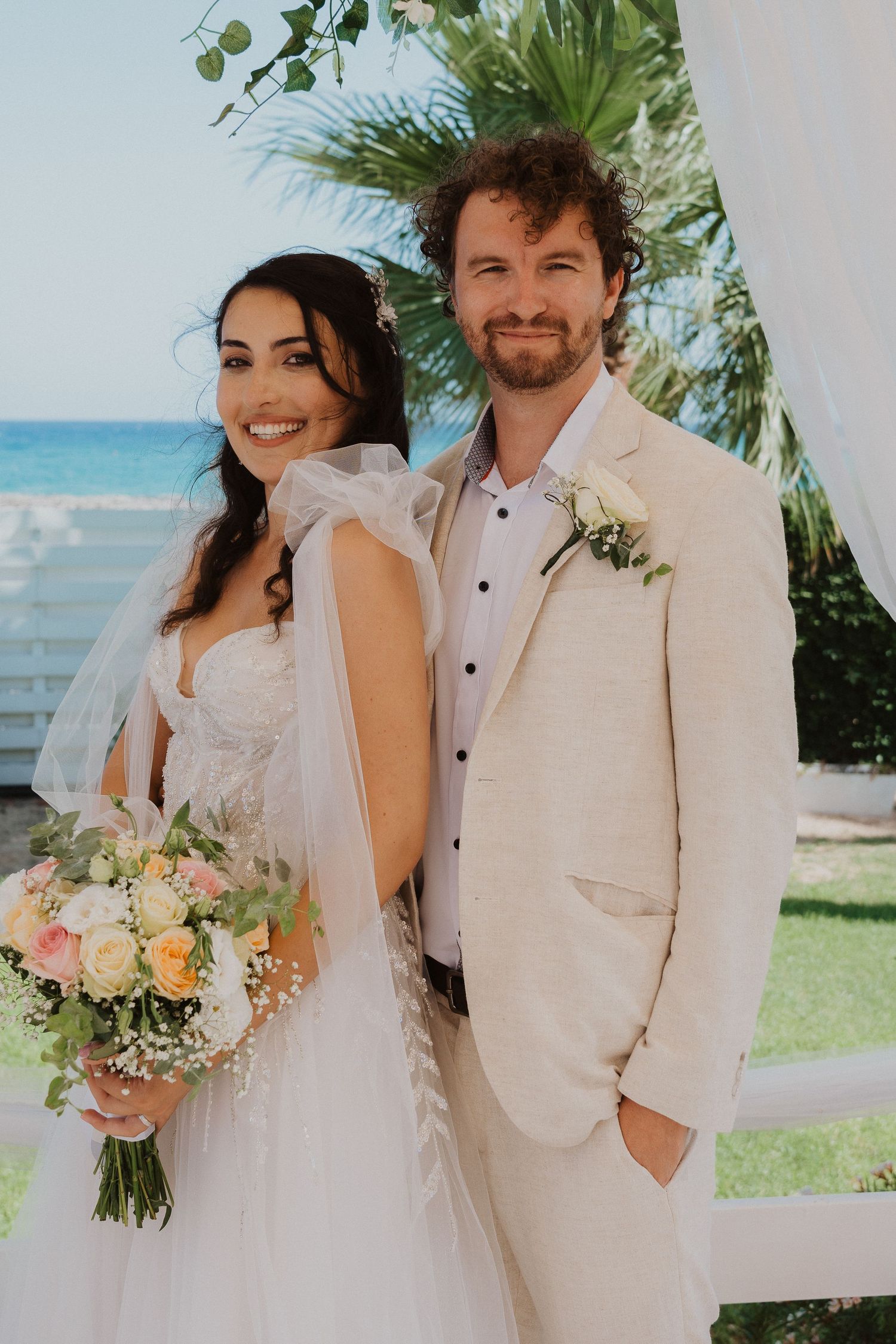 Wedding couple poses at beachfront venue under tropical foliage and flowers.