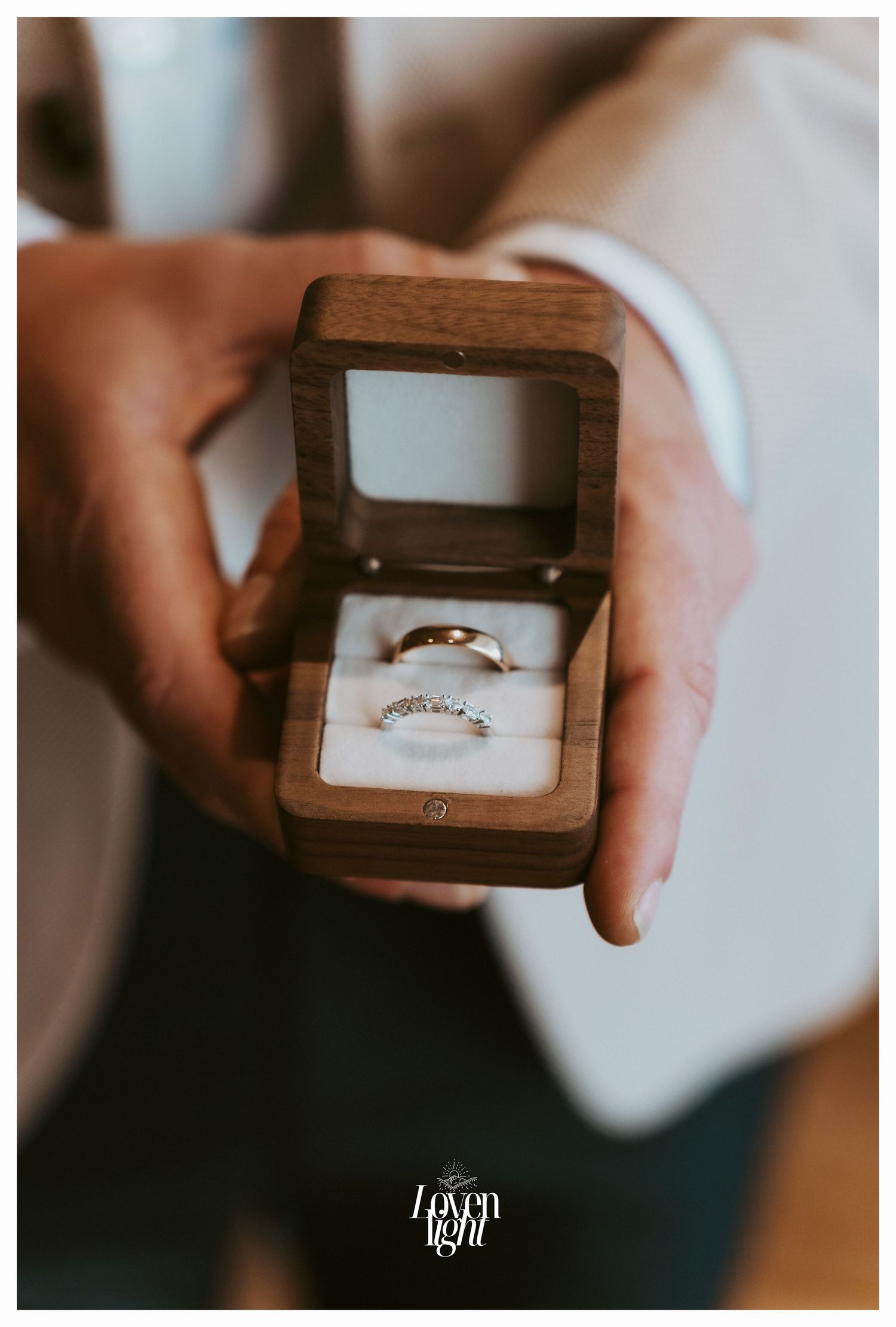 A wooden ring box displaying elegant wedding bands nestled on white cushioning.