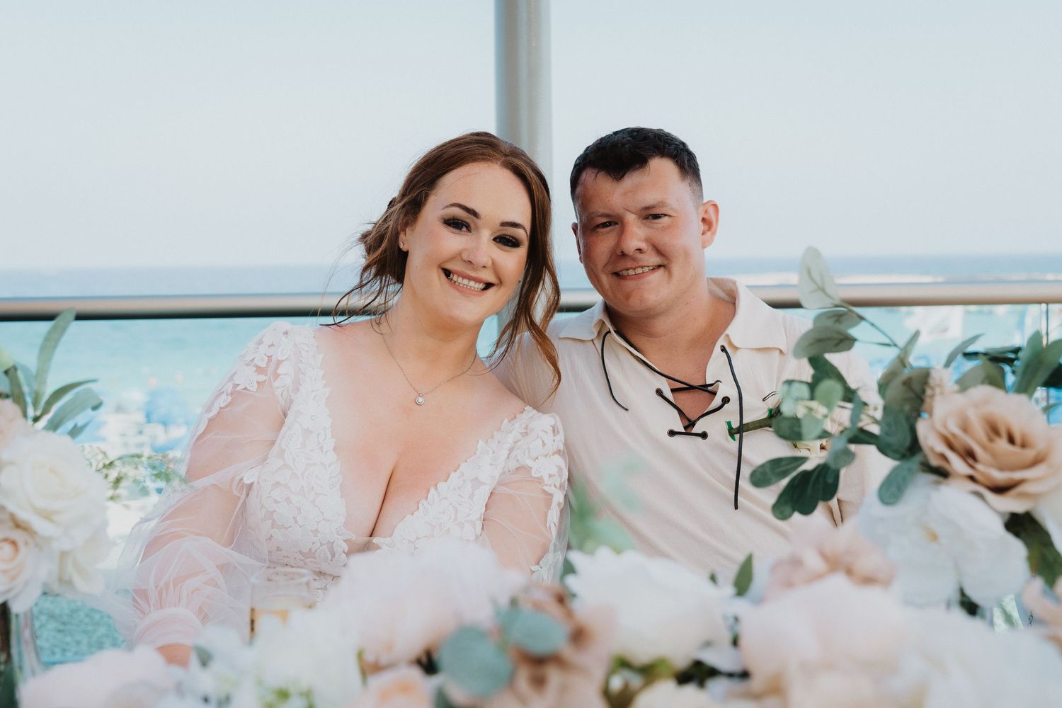 Seaside wedding portrait with floral decorations and ocean backdrop.