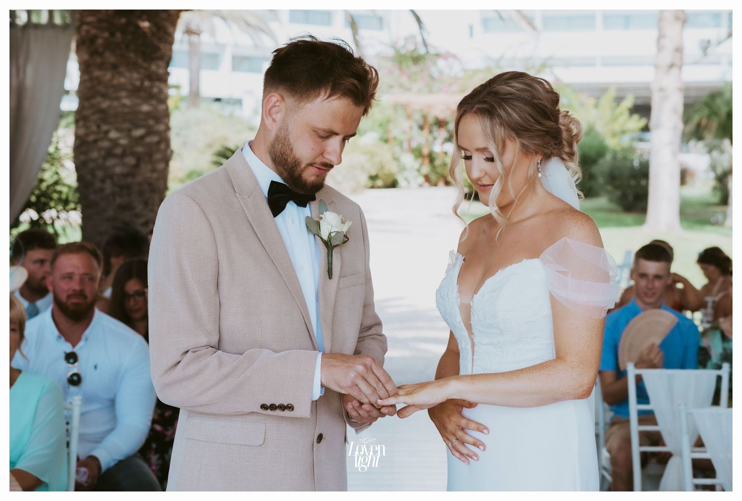 A wedding ring exchange captured during an outdoor ceremony with palm trees in background.