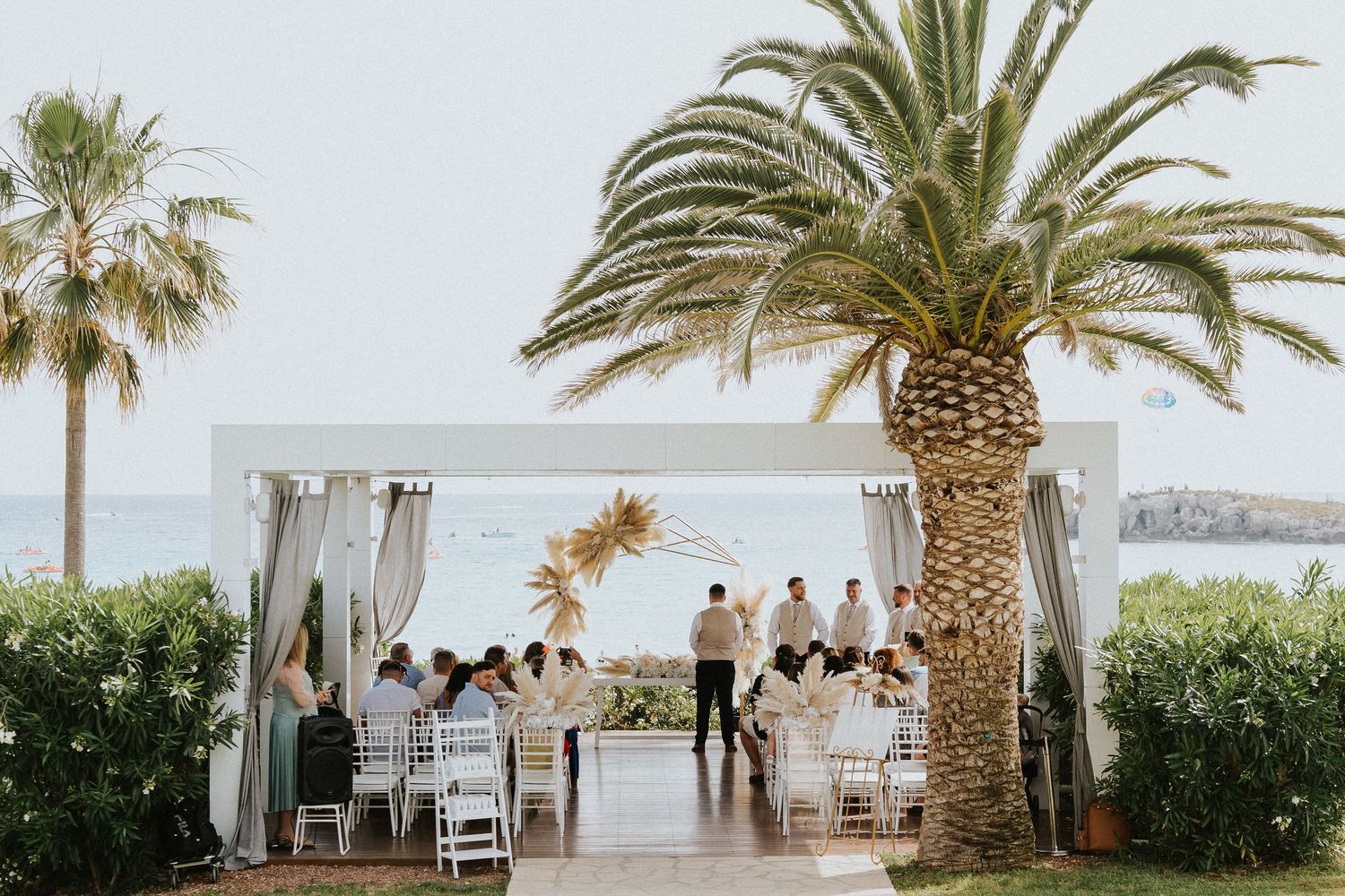 Beachside wedding ceremony setup with palm trees and draped white canopy.