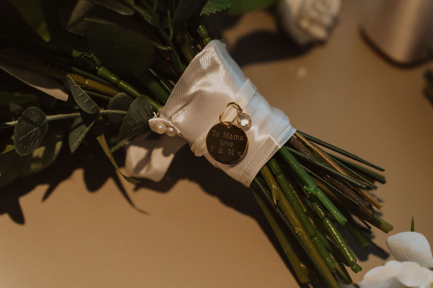 A decorative charm or locket attached to a wedding bouquet with white ribbon.