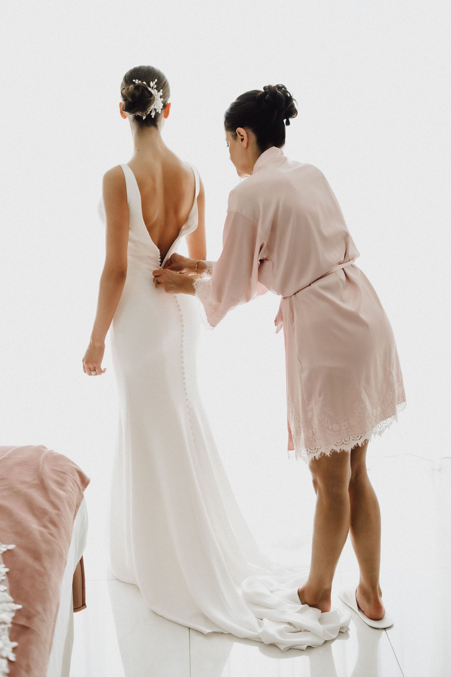 Back view of white wedding gown being adjusted with buttons and details.