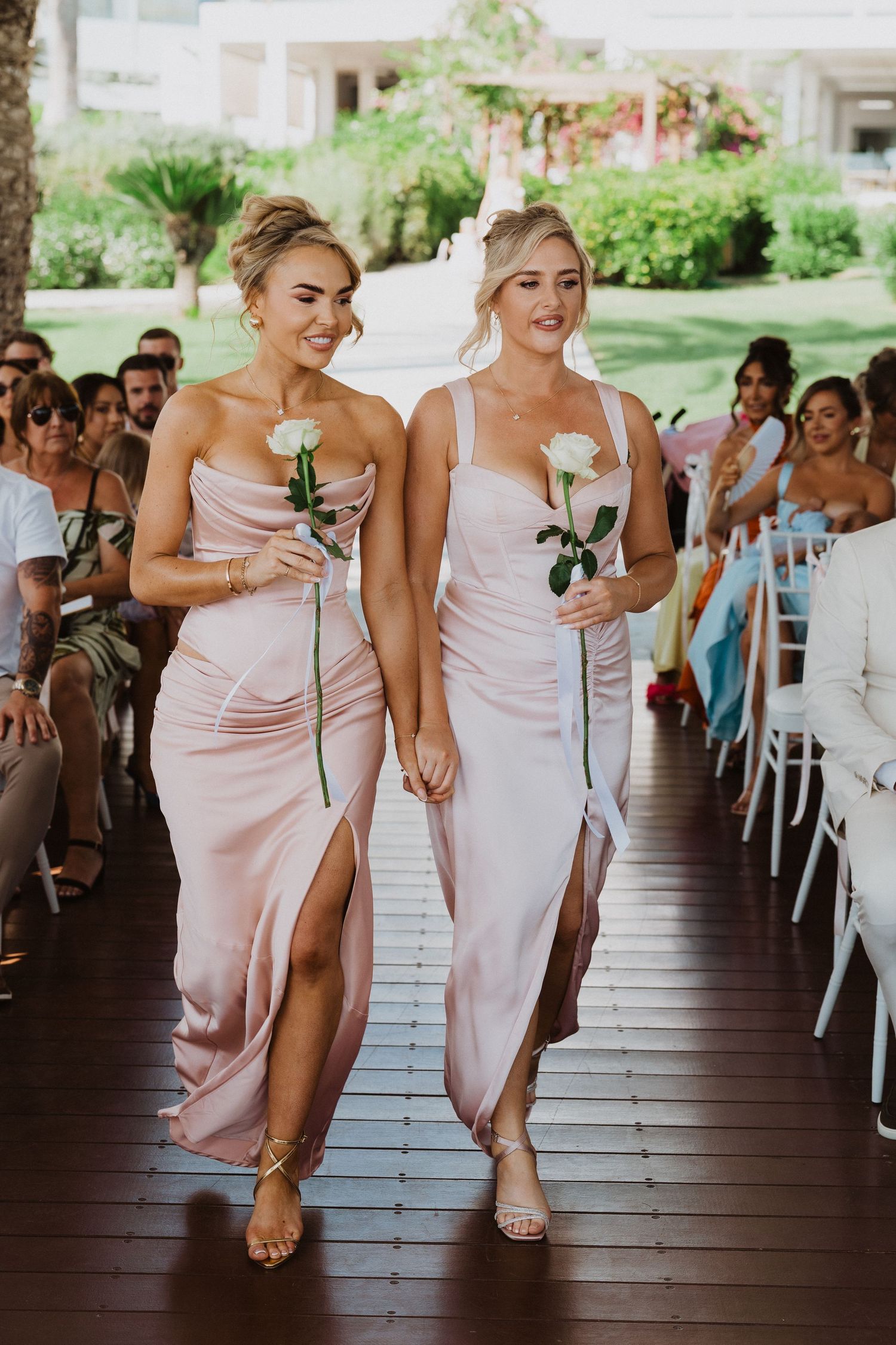 Bridesmaids in blush pink dresses walk in line down a covered outdoor walkway at a wedding venue.