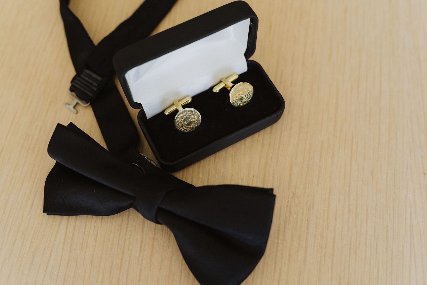 Black bow tie and gold cufflinks in a gift box on a wooden surface for a formal wedding.