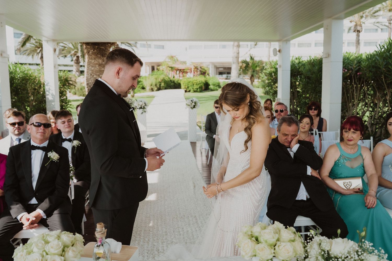 Bride and groom exchanging vows at outdoor wedding ceremony with guests.