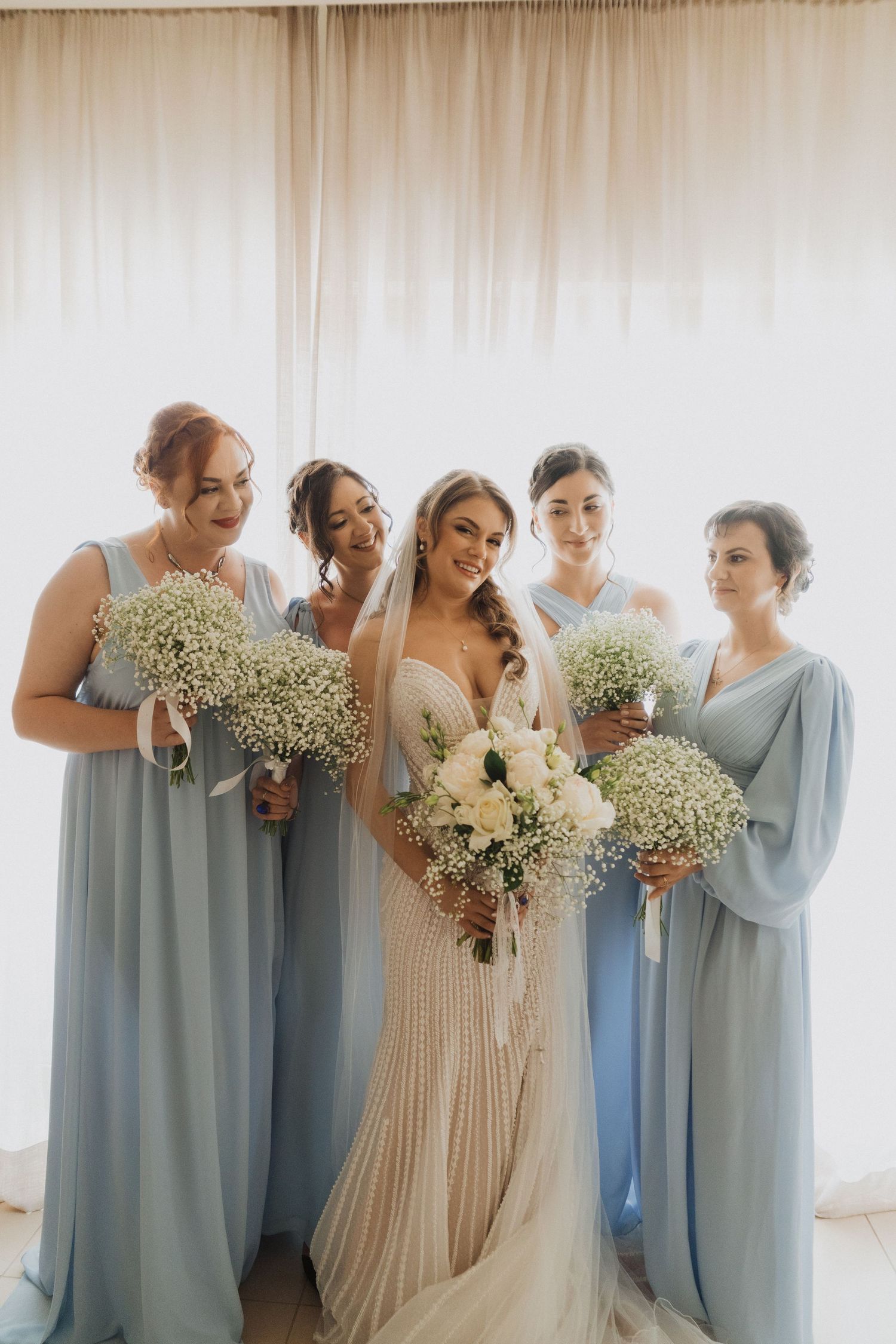 Bride in beaded gown with four bridesmaids in light blue dresses holding baby's breath bouquets.