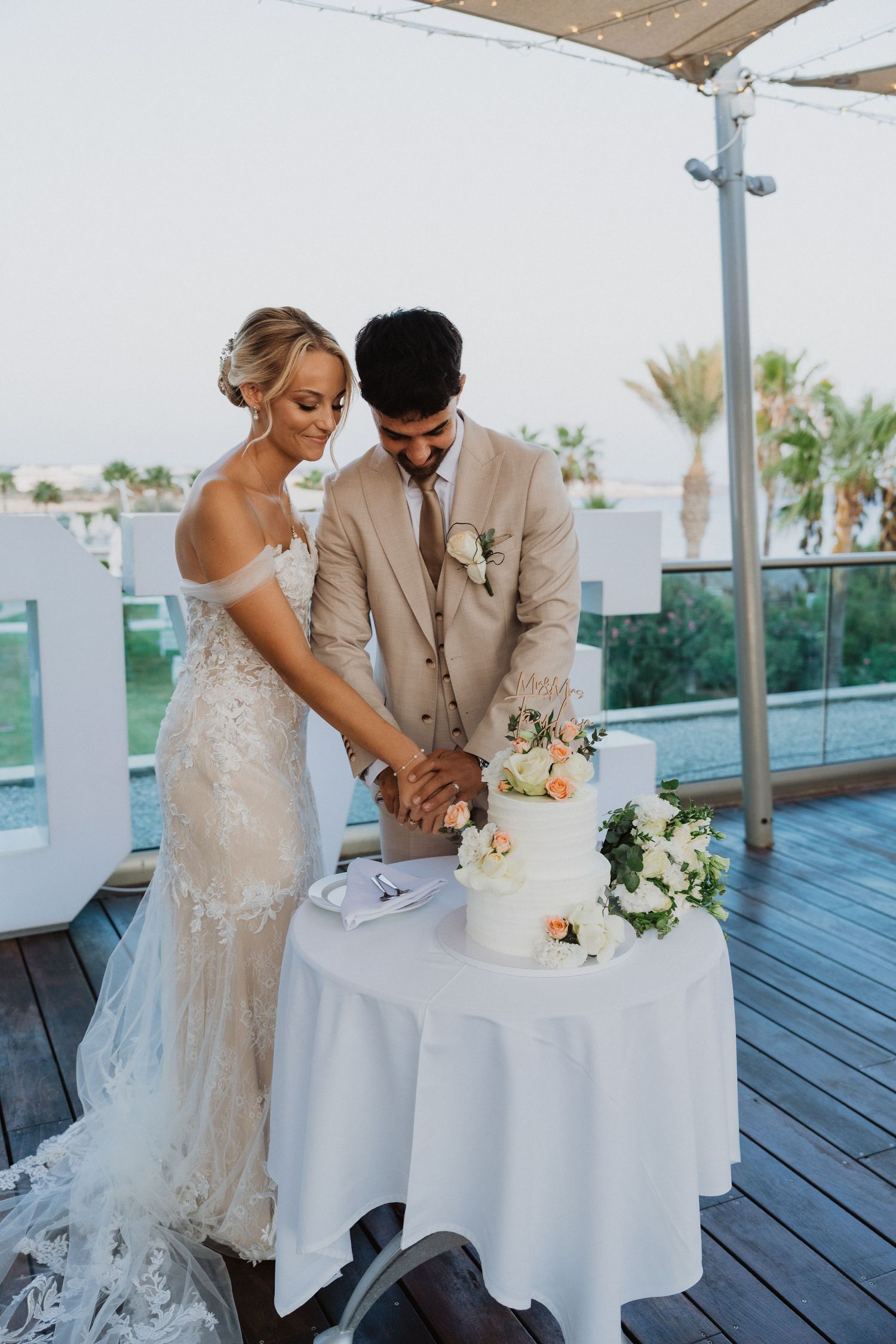 Couple cutting their white wedding cake on outdoor deck.