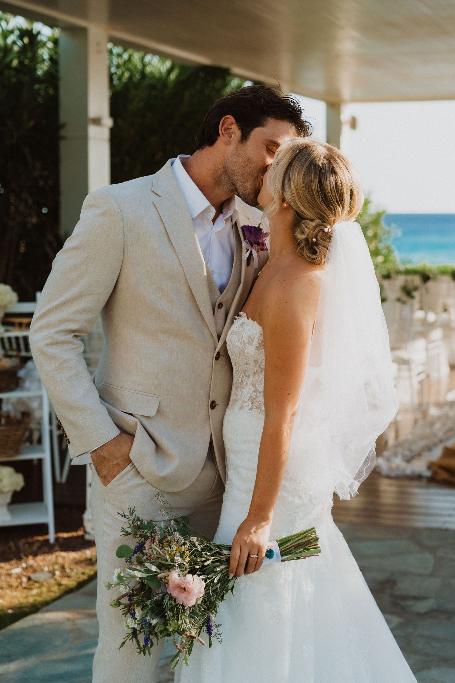 Newlyweds share tender moments during their beachside wedding photoshoot under covered patio.