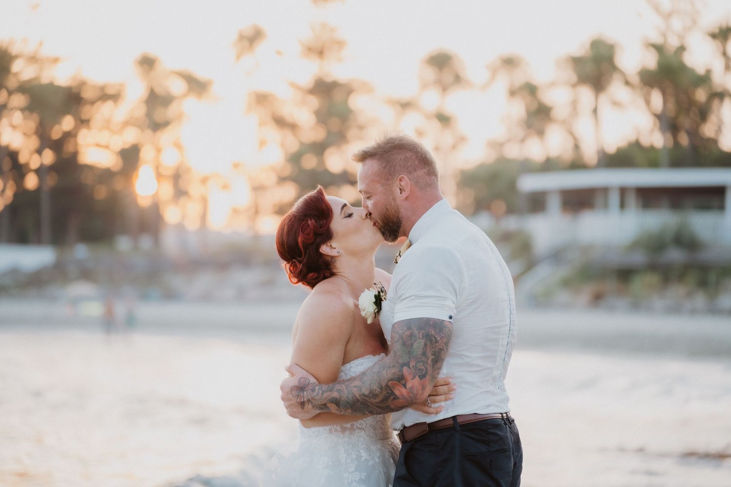 A romantic beach wedding moment at sunset with a couple in white and black attire.