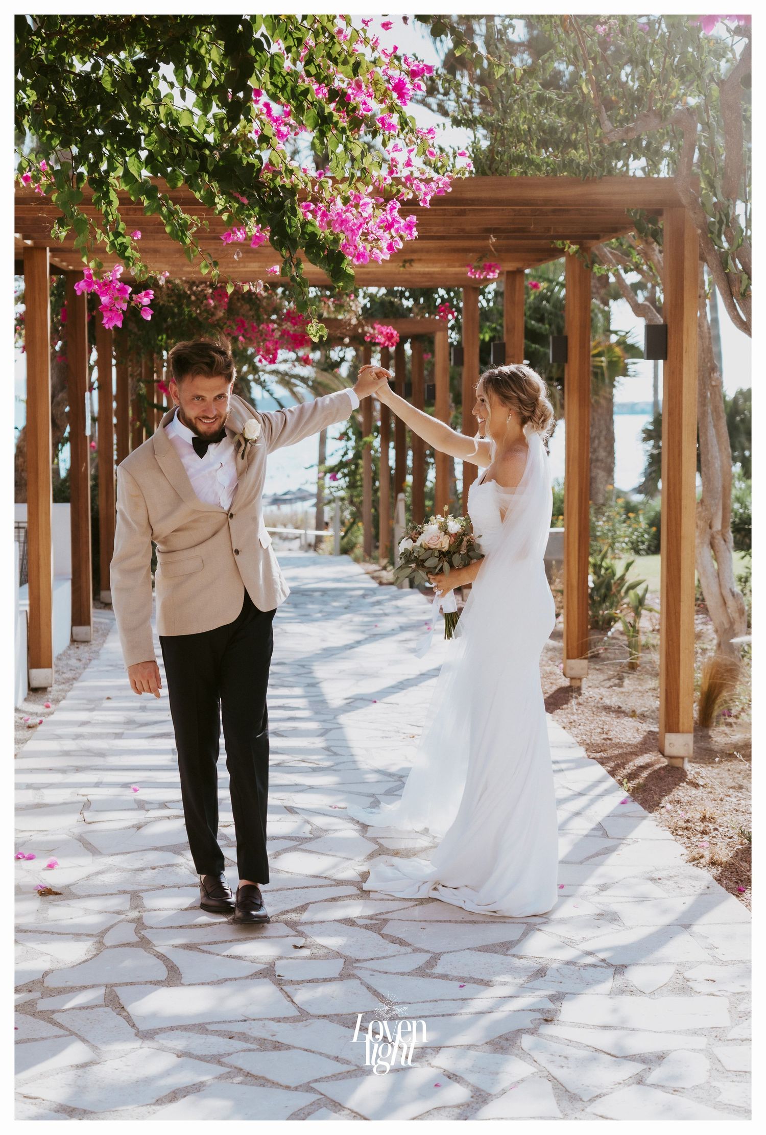 Newlyweds dance and twirl beneath a pergola covered in bright pink flowering vines.